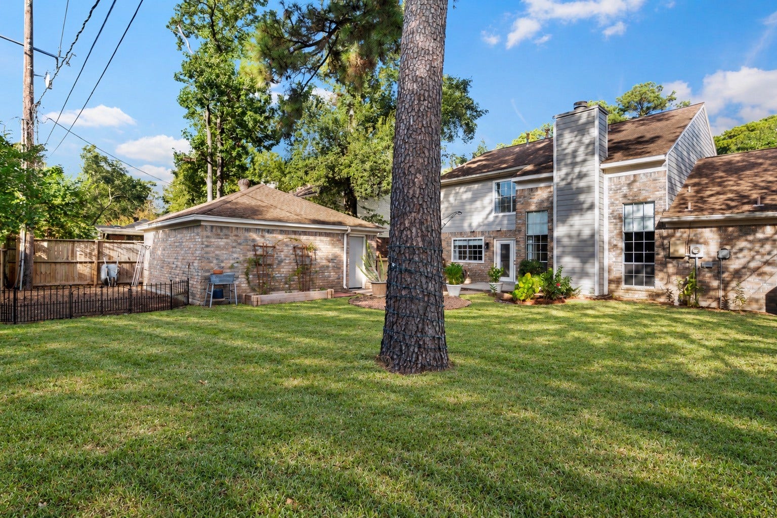 2631 Woodsboro Drive, Spring, TX 77388 Spacious backyard with lush grass and mature trees, offering a serene setting alongside a charming brick and siding home with large windows for natural light.