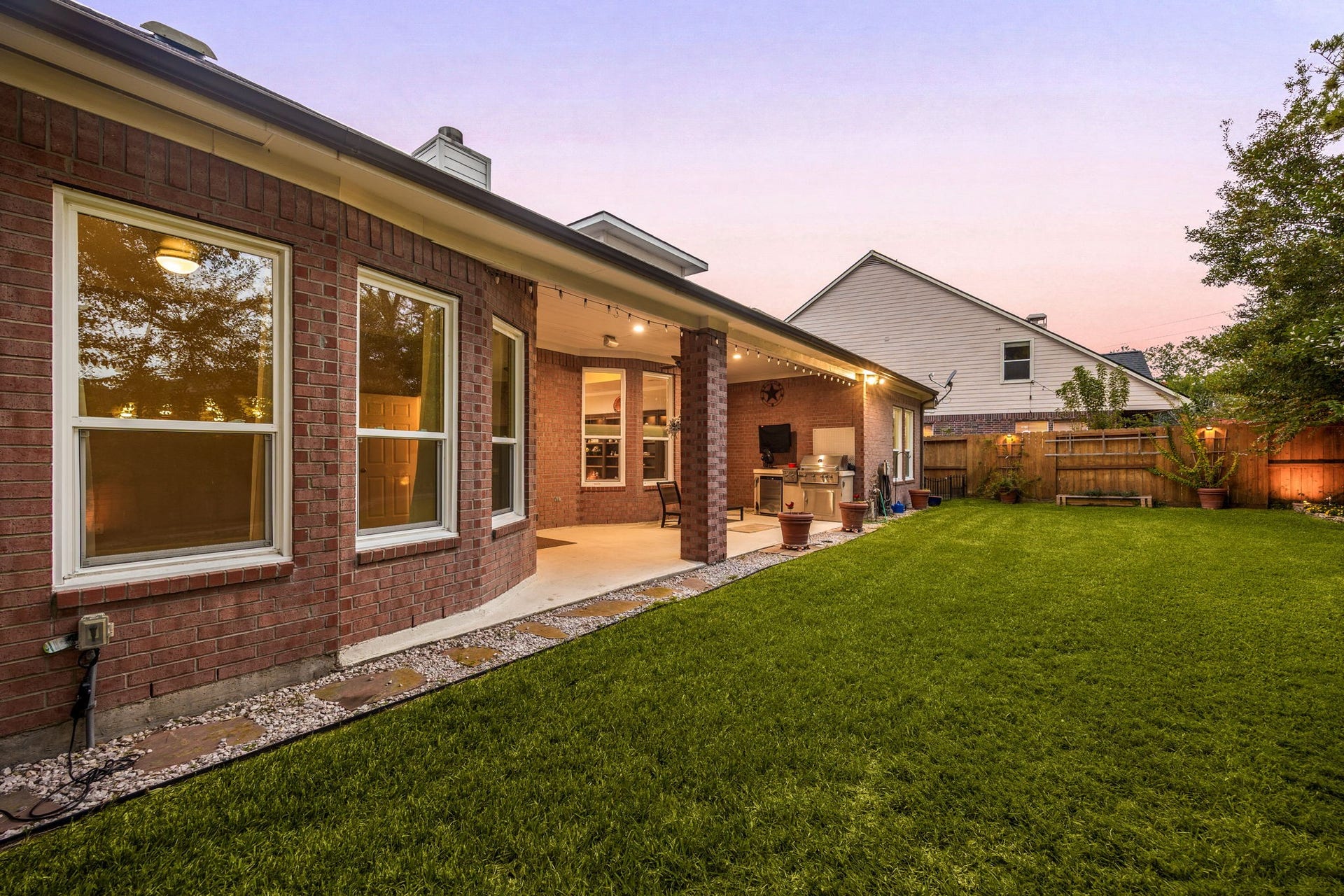 4110 Garden Cove Court, Katy, TX 77494 This view showcases the impressive length of the covered outdoor living space, framed by a sprawling, beautifully manicured green lawn. The combination of classic full-brick elevation, glowing interior windows, and a peaceful evening sky perfectly highlights the exceptional size and premium outdoor lifestyle this Cinco Ranch property provides.