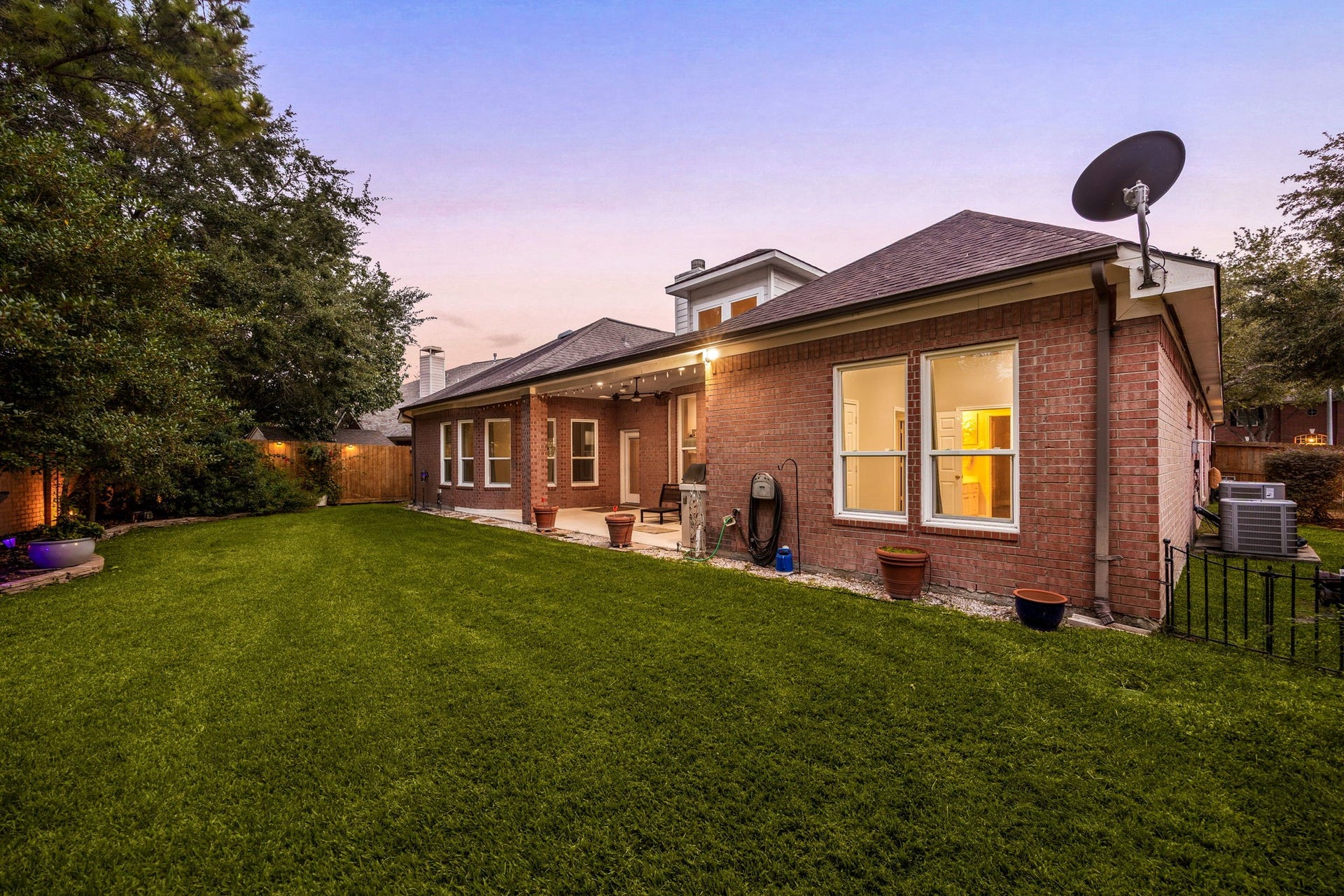 4110 Garden Cove Court, Katy, TX 77494 This view showcases the impressive length of the covered outdoor living space, framed by a sprawling, beautifully manicured green lawn. The combination of classic full-brick elevation, glowing interior windows, and a peaceful evening sky perfectly highlights the exceptional size and premium outdoor lifestyle this Cinco Ranch property provides.