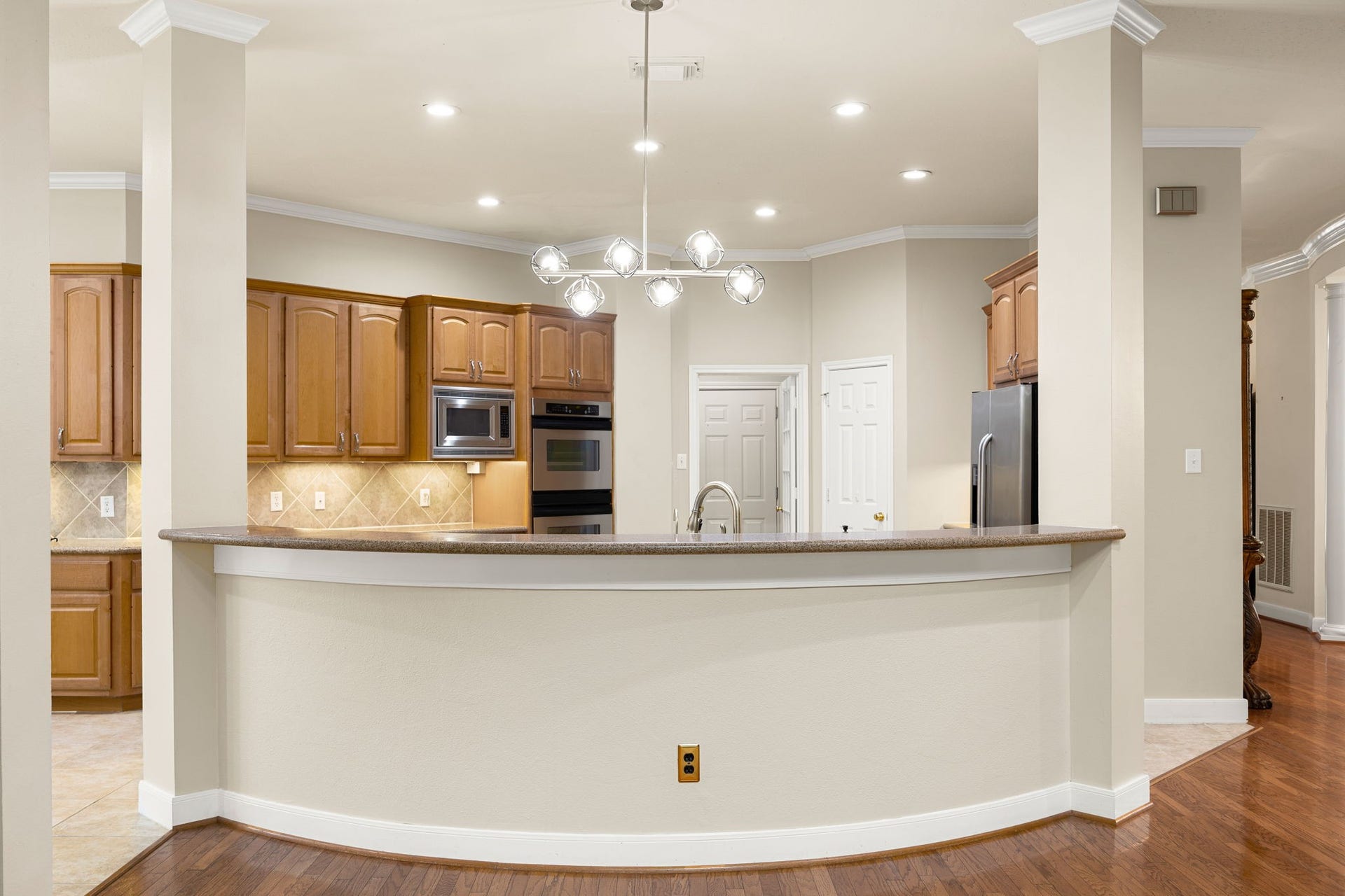 4110 Garden Cove Court, Katy, TX 77494 This stunning gourmet kitchen features rich wood cabinetry, built-in stainless steel appliances, and premium recessed lighting. The dramatic, curved breakfast bar overlooks the living spaces, anchored by an elegant, modern branching chandelier that adds a sophisticated touch to the home's open-concept design.