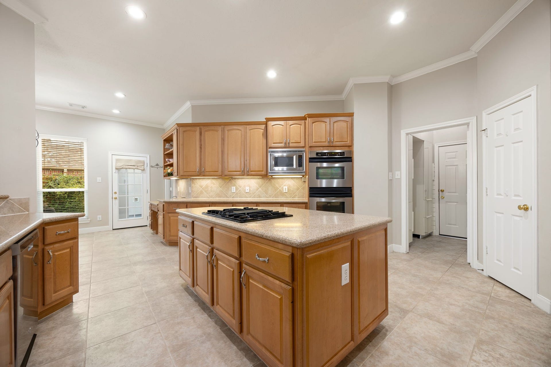 4110 Garden Cove Court, Katy, TX 77494 This viewpoint emphasizes the premium built-in stainless steel double ovens and matching microwave seamlessly integrated into the custom cabinetry. Bright recessed lighting combined with under-cabinet task lighting illuminates the polished solid-surface countertops, while a convenient backyard exit door keeps outdoor grilling within arm's reach.