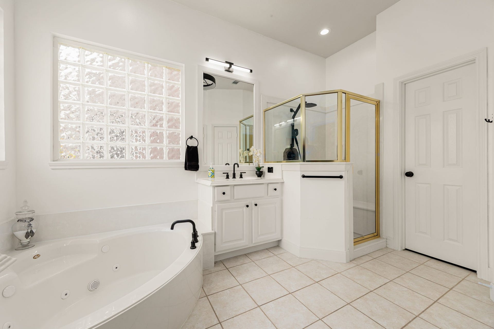 4110 Garden Cove Court, Katy, TX 77494 The primary bathroom is a serene oasis featuring a deep, separate jetted soaking tub nestled beneath a bright privacy-glass block window. Complete with a spacious walk-in shower, bright white vanity cabinetry, elegant modern fixtures, and crisp tile flooring, it offers the perfect space to unwind and recharge.