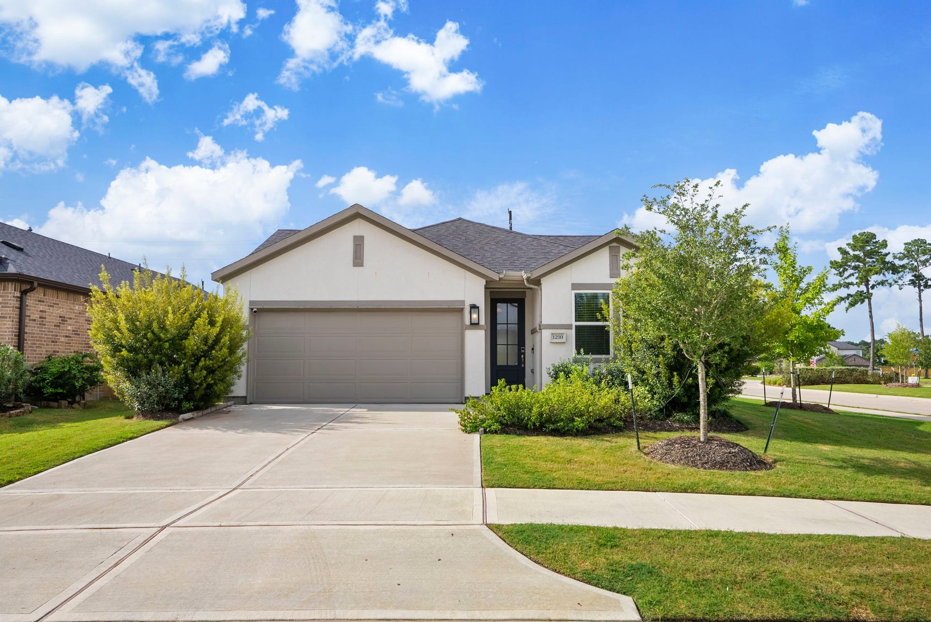 This photo showcases a modern, single-story home with a two-car garage. It features a neatly landscaped front yard and a clean driveway. The house has a light exterior with a dark roof, creating an inviting curb appeal.