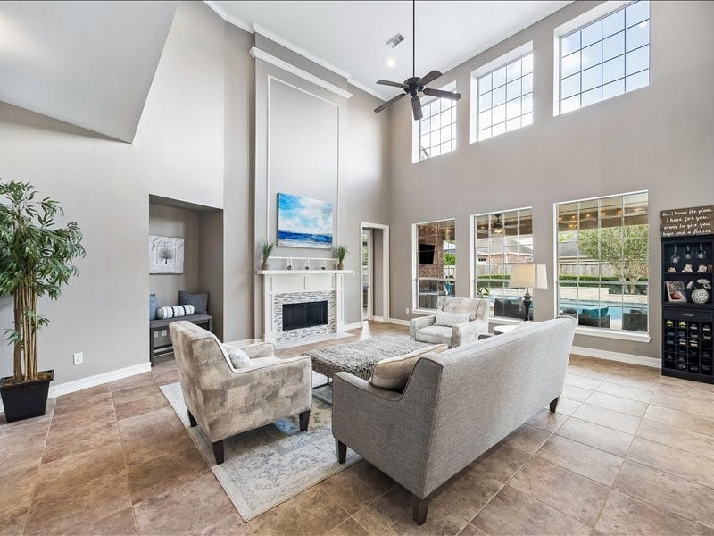 9007 Avebury Stone Circle, Missouri City, TX 77459 The family room's elegant stone fireplace anchors the space beautifully, framed by tall windows, neutral tones, plush seating, and sparkling pool views beyond, creating a warm and inviting gathering space for every season.