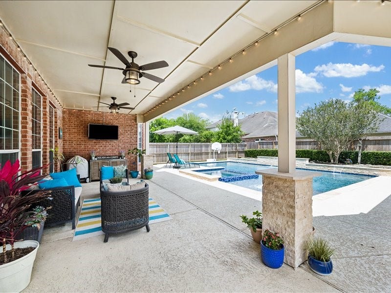 9007 Avebury Stone Circle, Missouri City, TX 77459 Entertain in style under this expansive covered back patio featuring dual ceiling fans, string lights, an outdoor wall-mounted TV, and comfortable patio furniture. The perfect bridge between indoor comfort and the stunning pool oasis just beyond.