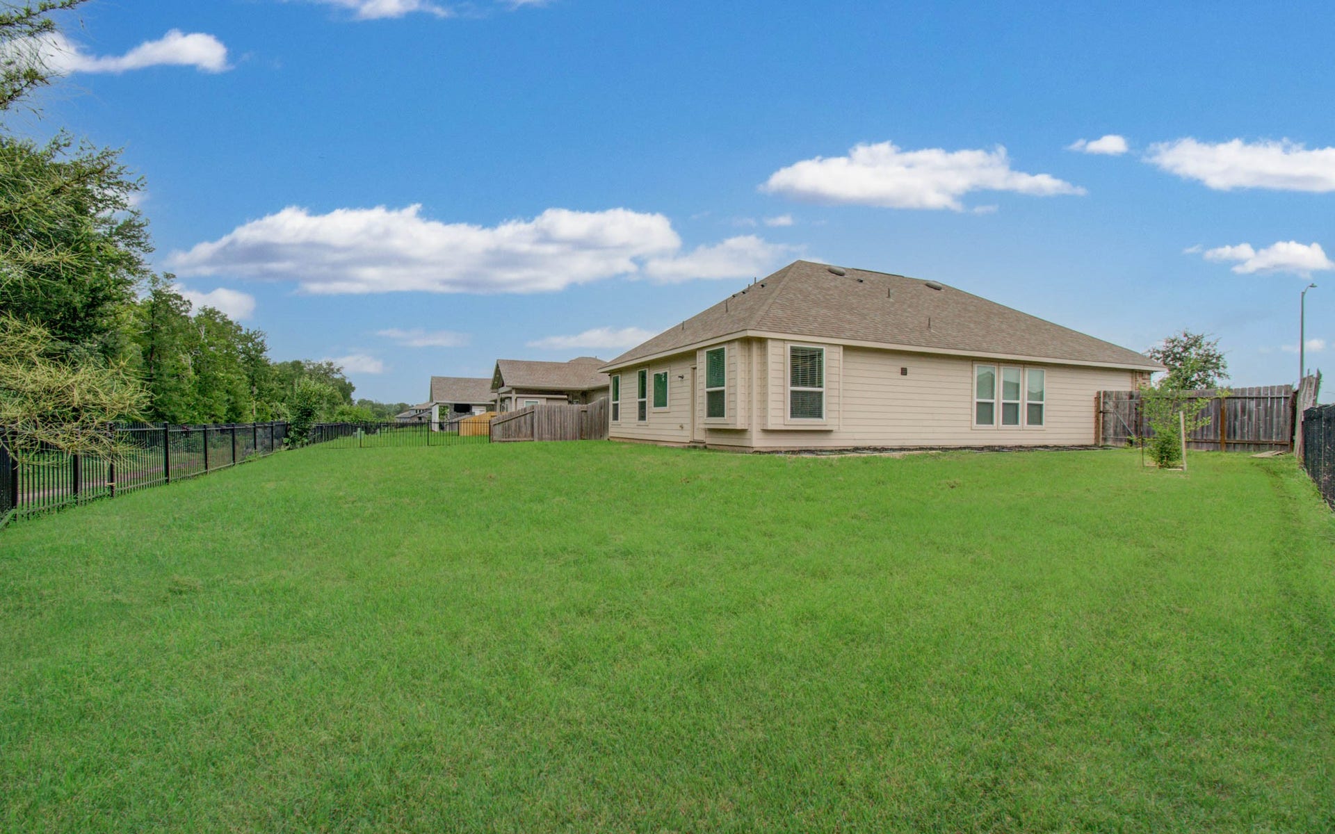 3403 Brazos Falls Dr, Richmond, TX 77469 Wide-open yard with a wrought iron fence and mature trees along the back.