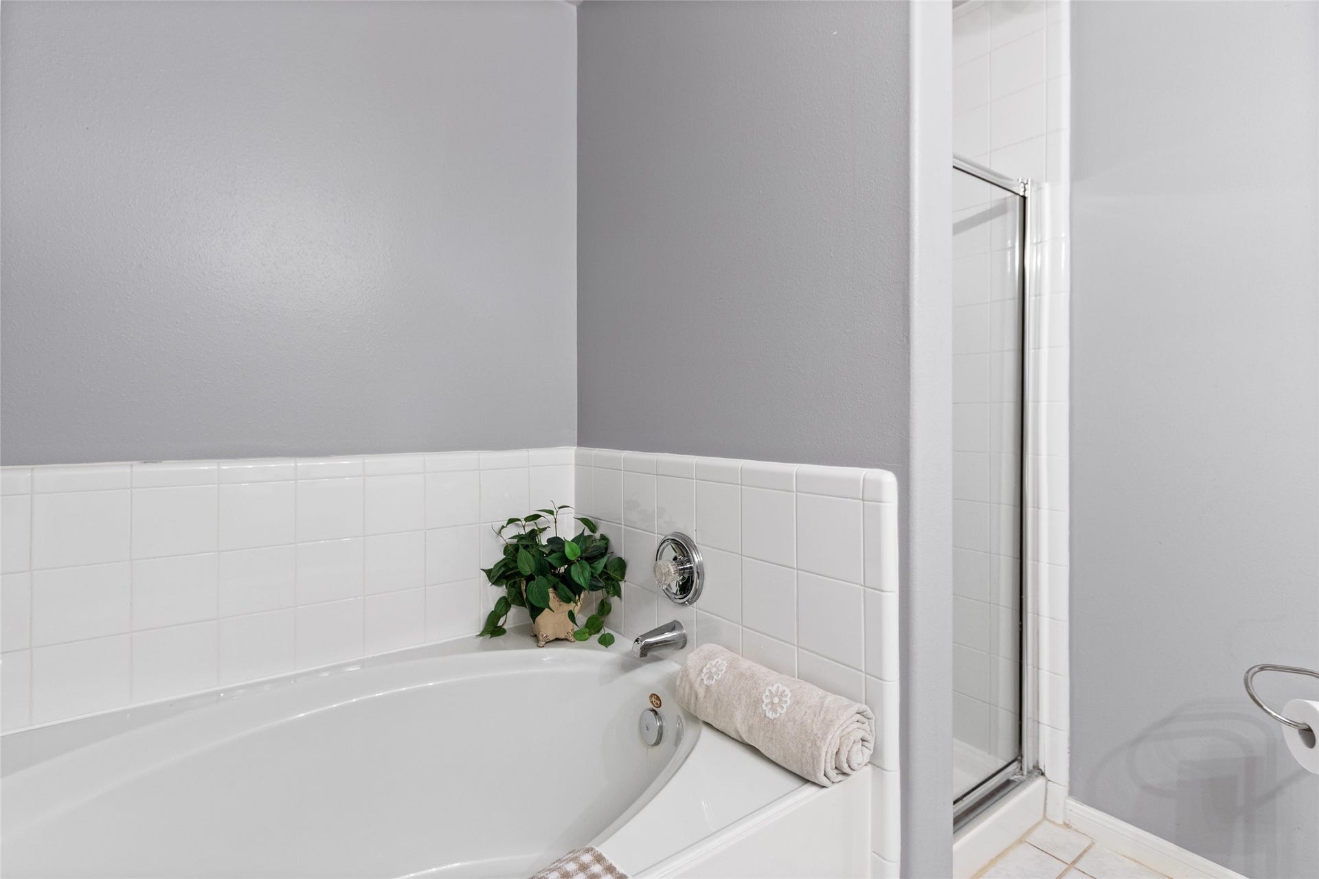 3001 Meadow Bay Drive, Dickinson, TX 77539 A stylish bathroom features a spacious bathtub with elegant white tile surround and a separate shower, accented by a soothing gray wall for a relaxing ambiance.