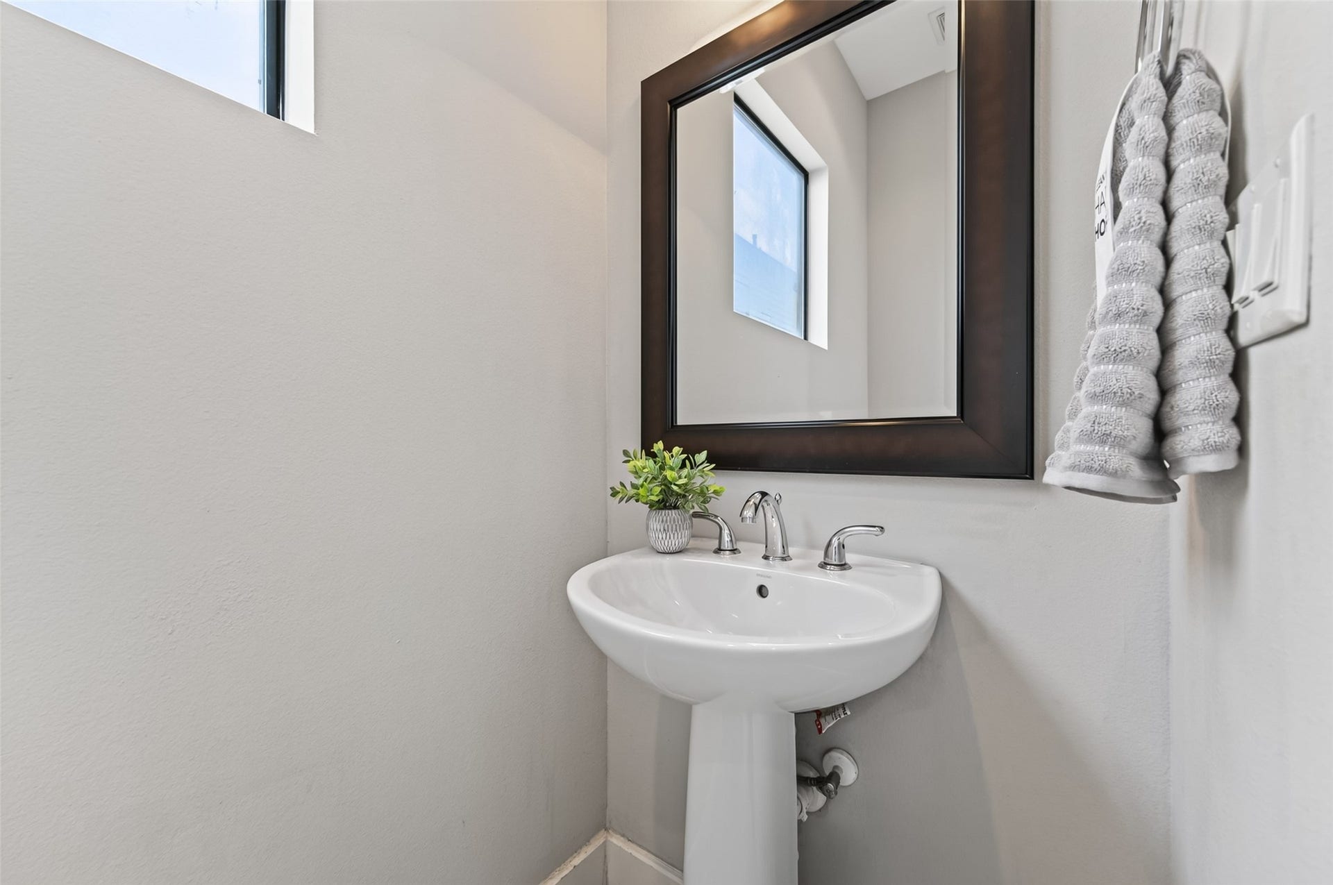 2805 Blodgett Street, #C, Houston, TX 77004 A chic powder room featuring a sleek pedestal sink, modern fixtures, and a large framed mirror, complemented by a bright window and elegant towel display.