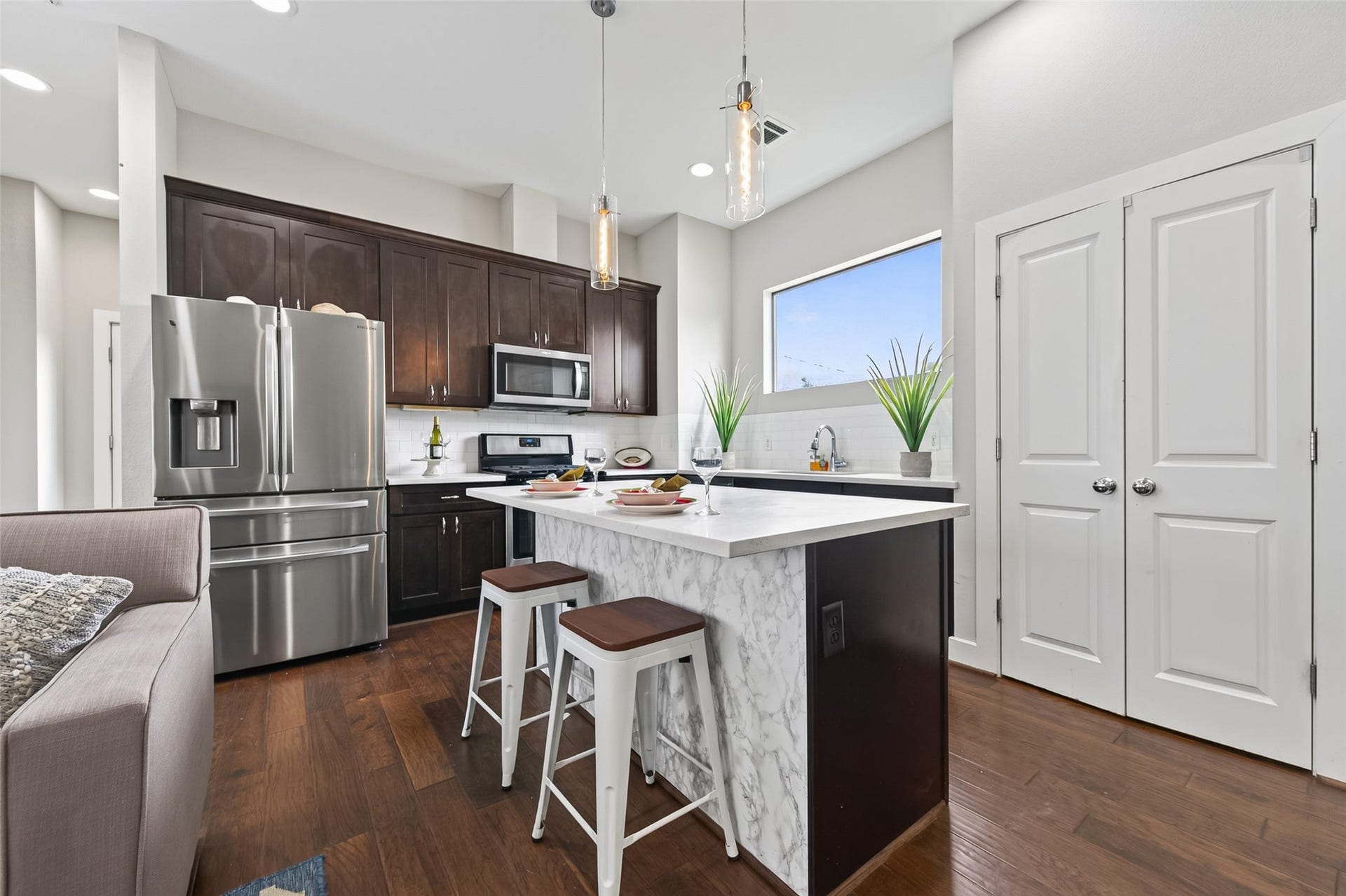 2805 Blodgett Street, #C, Houston, TX 77004 Modern open-concept living area with sleek kitchen, featuring stainless steel appliances, a large island with bar seating, and rich hardwood floors, complemented by a cozy seating area and plenty of natural light.