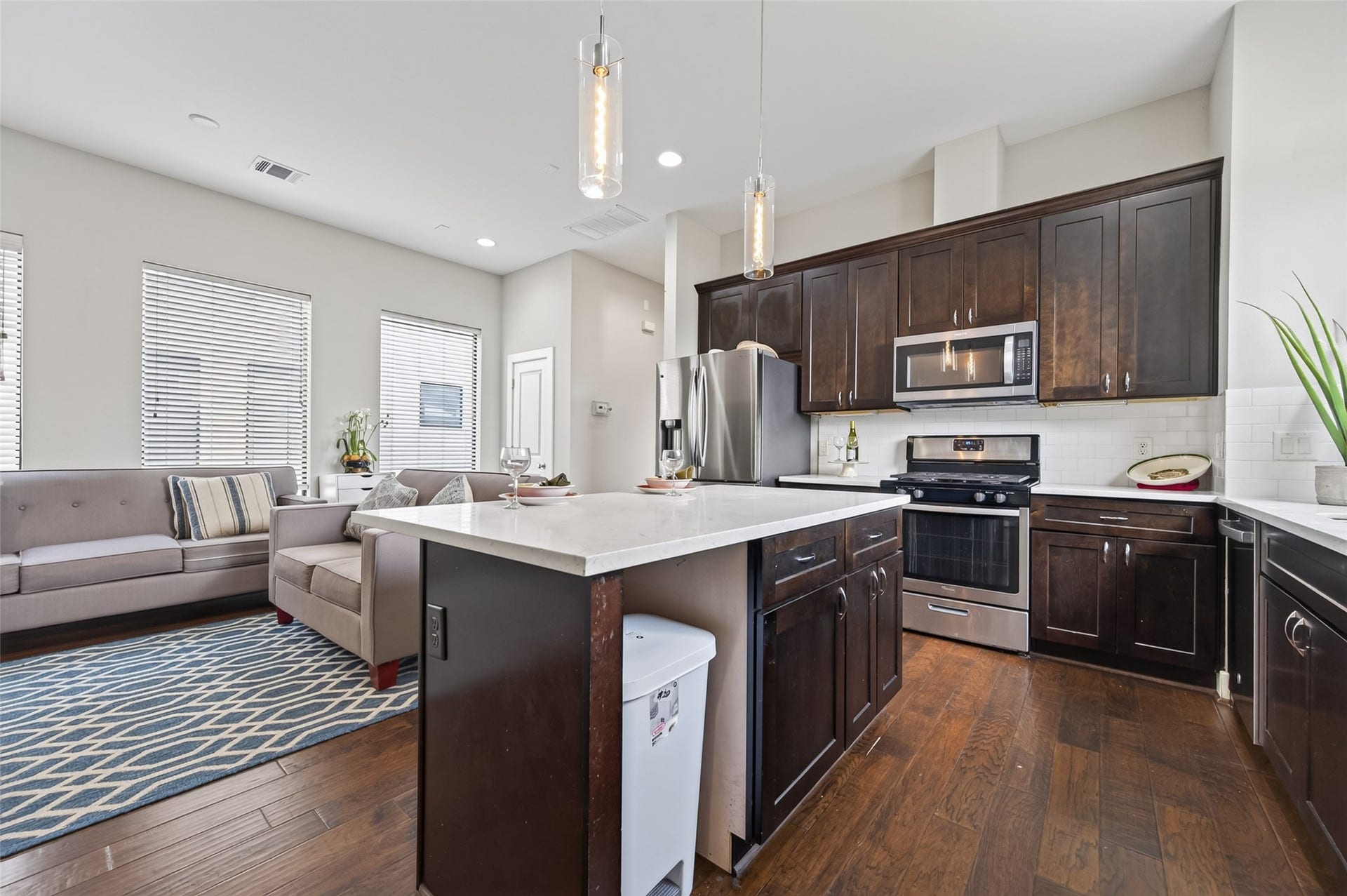 2805 Blodgett Street, #C, Houston, TX 77004 Modern kitchen with sleek stainless steel appliances, rich dark cabinetry, and a stylish marble island featuring seating for two. The space is accented by pendant lighting and a bright window, creating an inviting atmosphere.
