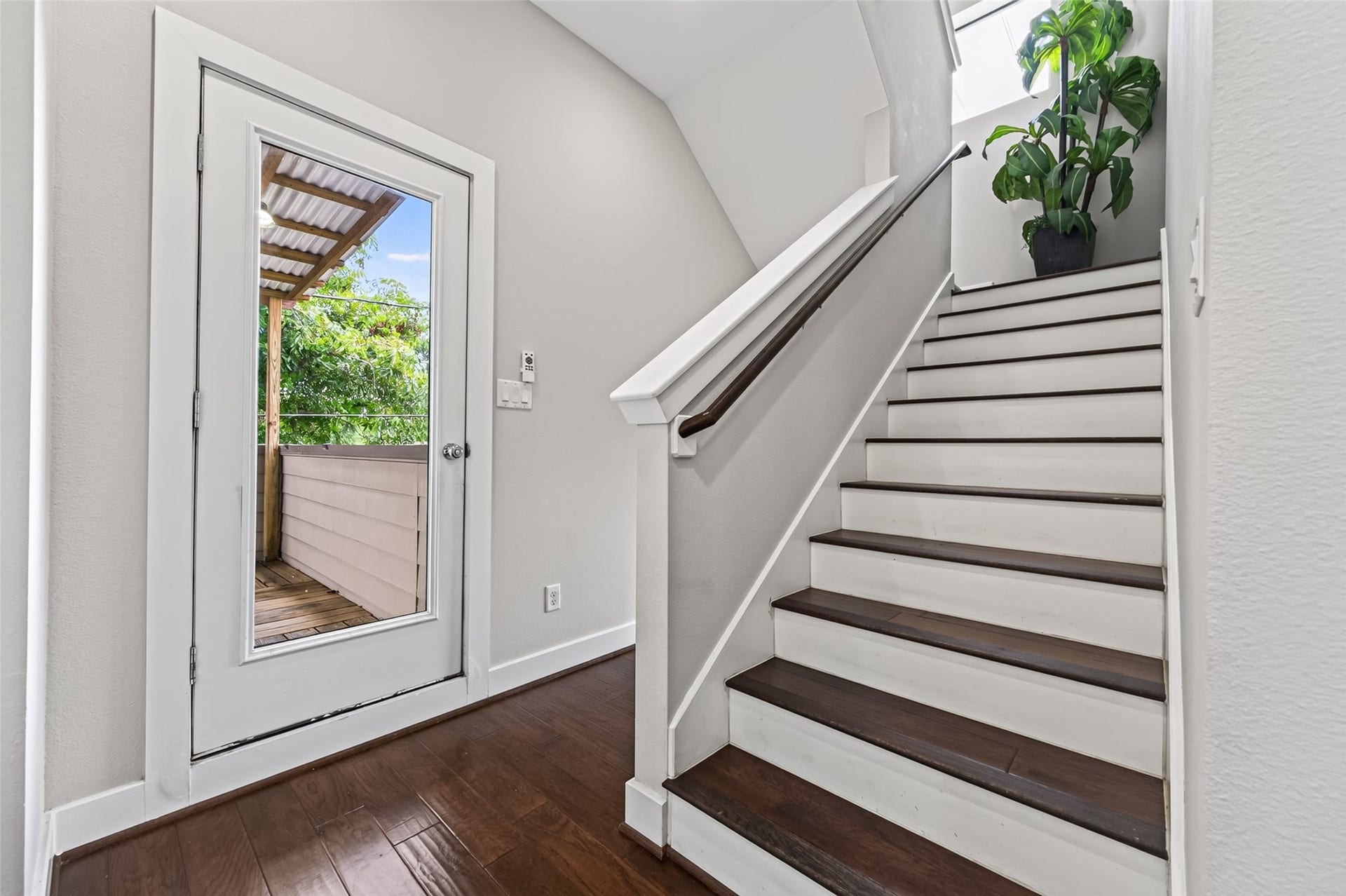 2805 Blodgett Street, #C, Houston, TX 77004 Bright entryway featuring elegant dark wood flooring, a sleek staircase with white accents, and a glass door leading to a cozy outdoor deck.