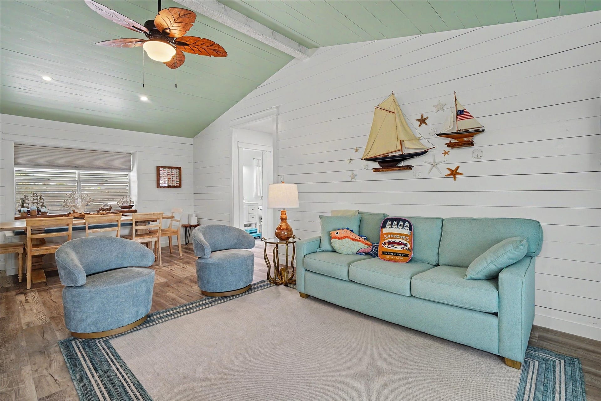 The living and dining areas come together in a beautiful open-concept space, featuring coastal-inspired colors, modern shiplap walls, a painted ceiling, and a statement beam that adds warmth and character