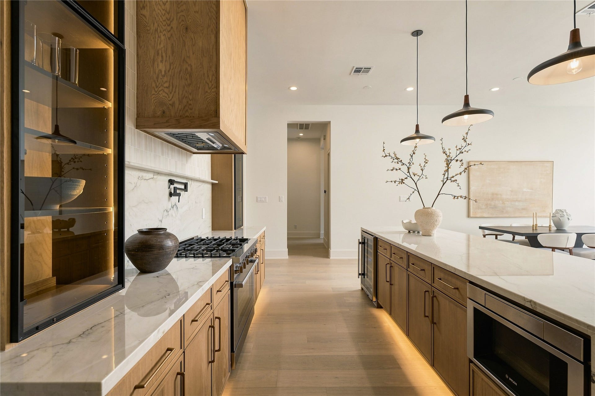 2109 McKean Drive, Houston, TX 77080 A dramatic perspective showcases the kitchens Midnight Glass Towers and illuminated cabinetry, creating a striking contrast against the warmth of the white oak finishes