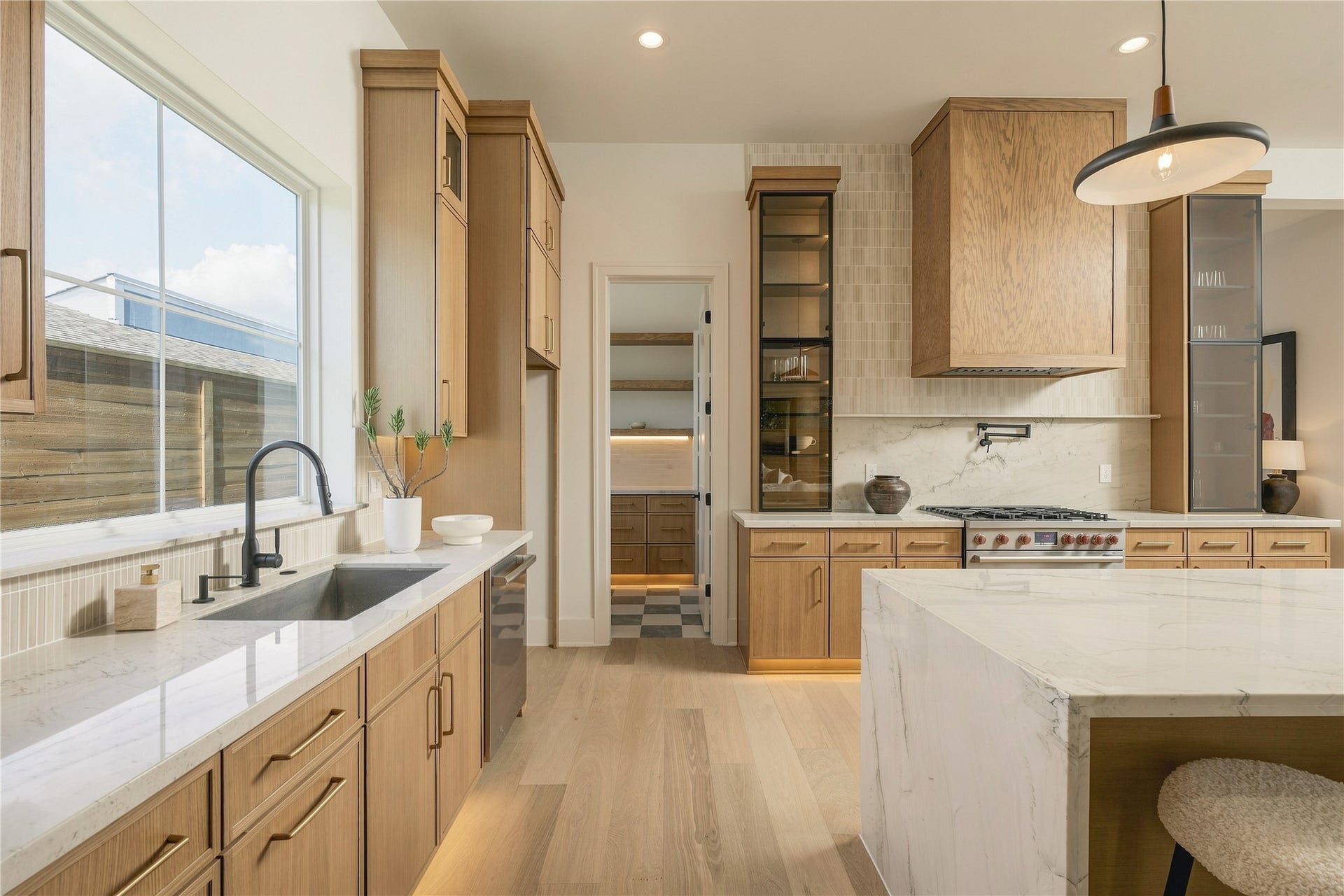 2109 McKean Drive, Houston, TX 77080 A closer view reveals the kitchens layered craftsmanship, where custom white oak details, glass-front cabinetry, and integrated LED lighting bring warmth and dimension to the space.