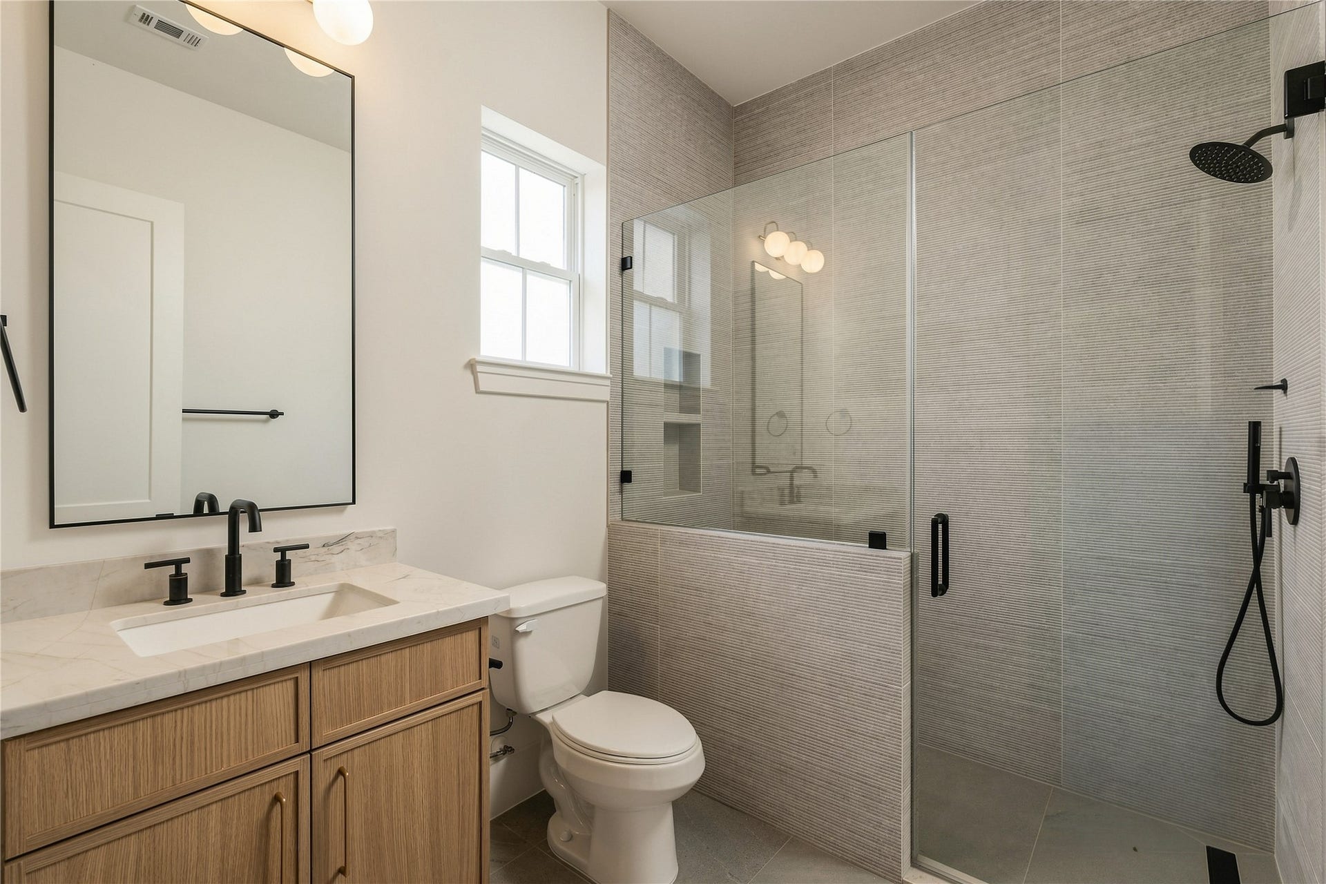 2109 McKean Drive, Houston, TX 77080 This secondary bath pairs Mount Blanc Quartzite with full-height designer tile and a frameless glass shower, creating a polished ensuite experience with finishes typically reserved for a primary suite.