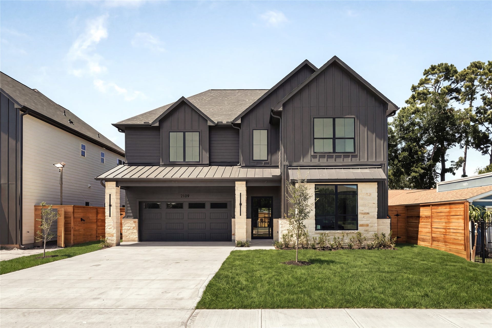 2109 McKean Drive, Houston, TX 77080 A commanding street presence introduces the home with limestone accents, custom wood detailing, and an 18-foot glass-panel garage door, balancing modern architecture with warm, natural materials.