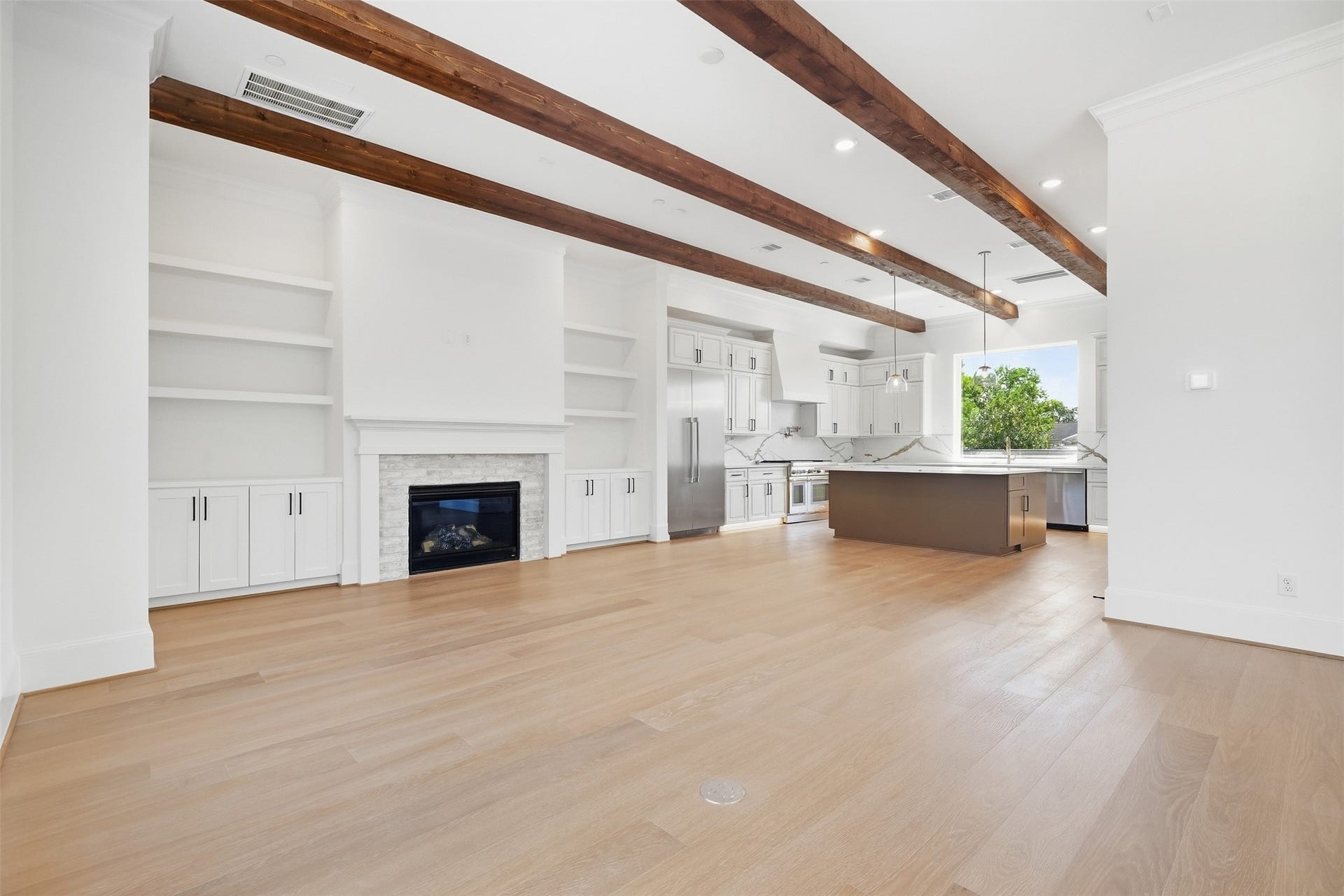 2111 Nantucket Drive, #D, Houston, TX 77057 The light-filled living room features exposed wood beams, a fireplace framed by built-in shelving and cabinetry, and oversized windows bringing in abundant natural light.