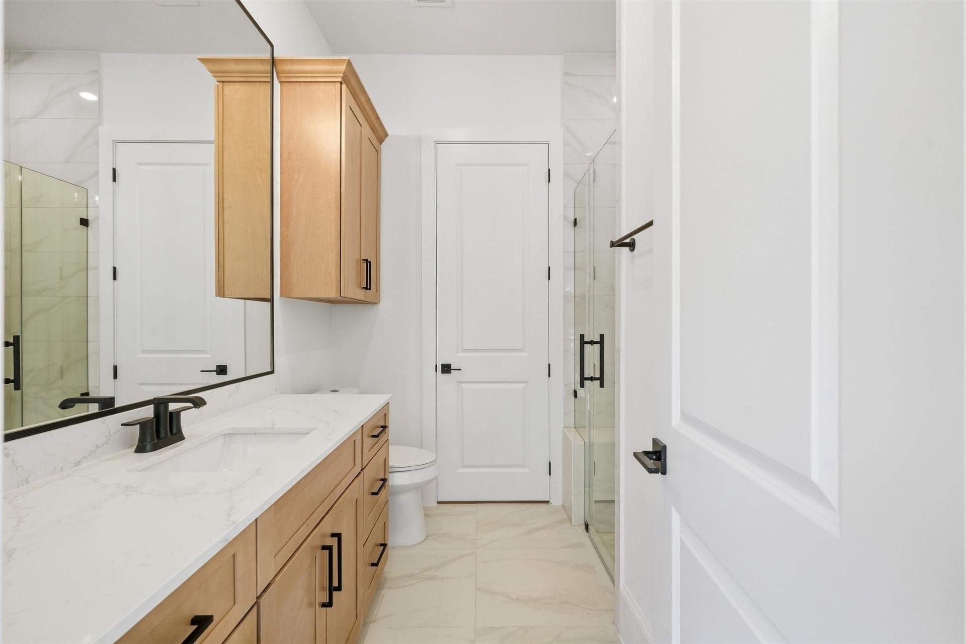 2111 Nantucket Drive, #D, Houston, TX 77057 The adjoining full bath features warm wood cabinetry, quartz counters, black fixtures, and a glass-enclosed walk-in shower.