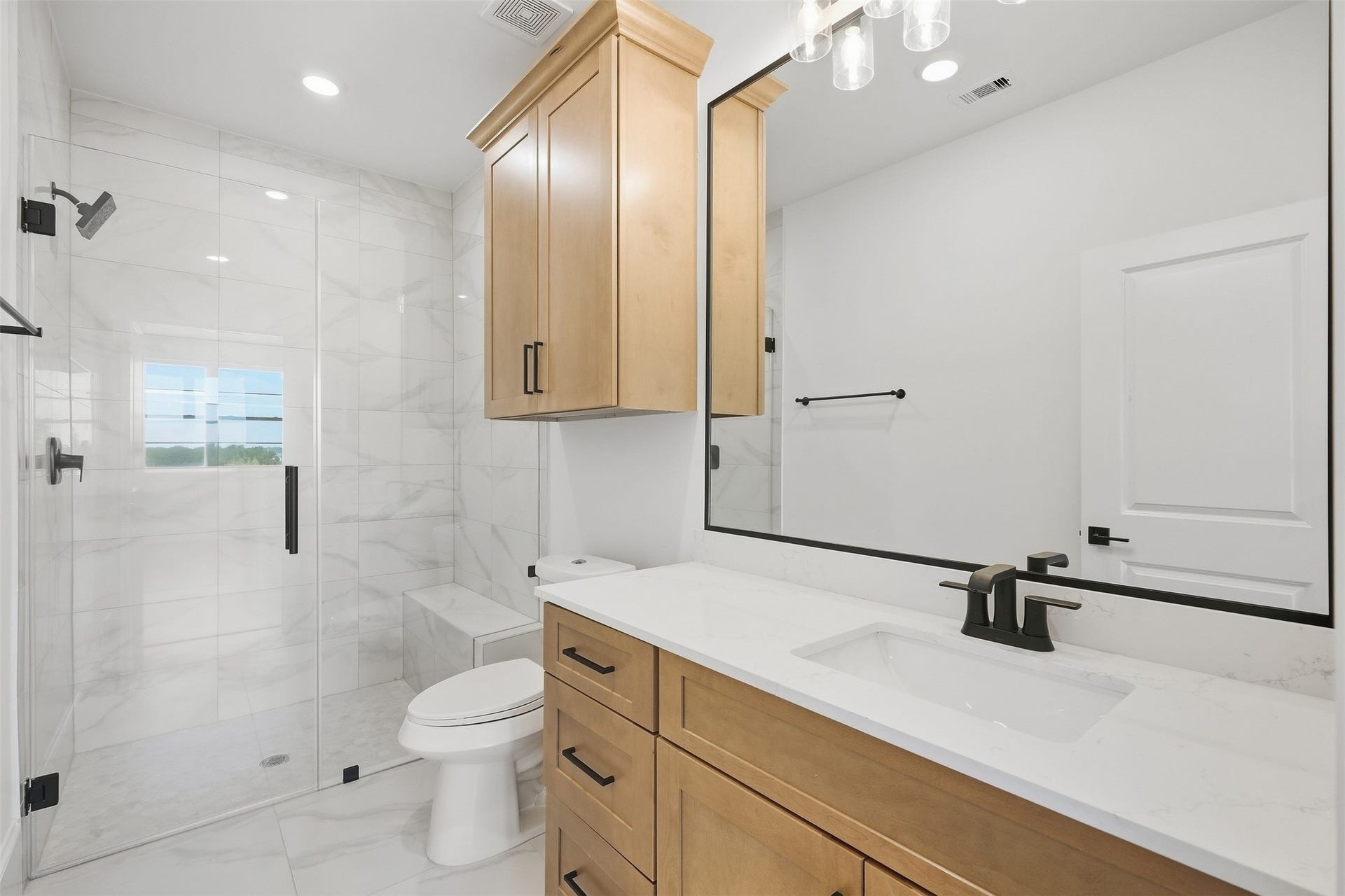 2111 Nantucket Drive, #D, Houston, TX 77057 The fourth-floor full bath features warm wood cabinetry, quartz countertops, black fixtures, and a glass-enclosed walk-in shower.