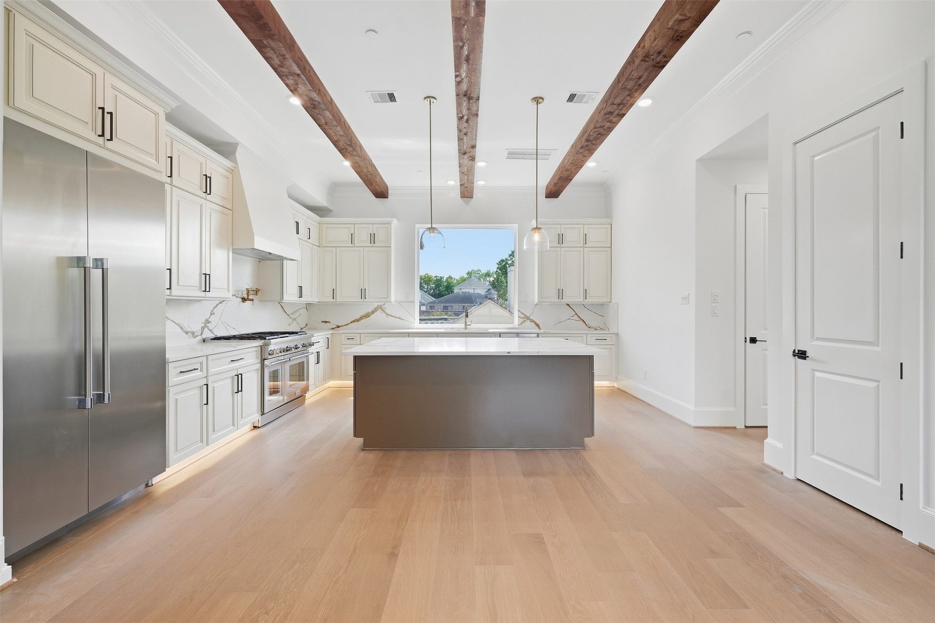 2111 Nantucket Drive, #D, Houston, TX 77057 The kitchen pairs warm cabinetry with quartz countertops and backsplash, stainless steel appliances, an oversized center island, and exposed wood beams overhead.