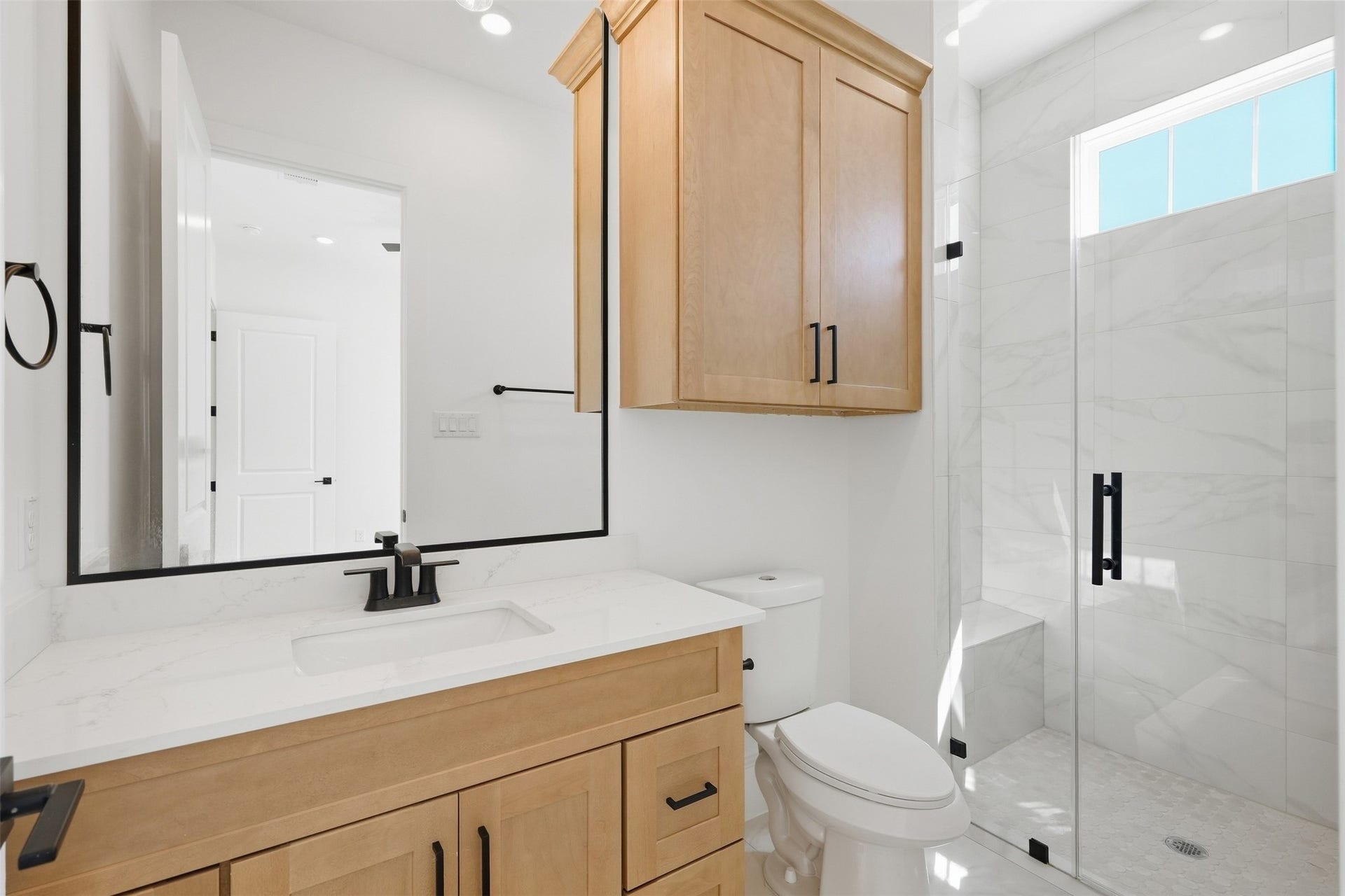 2111 Nantucket Drive, #D, Houston, TX 77057 The secondary en-suite bath features a walk-in shower, warm wood cabinetry, quartz countertops, and sleek black fixtures.