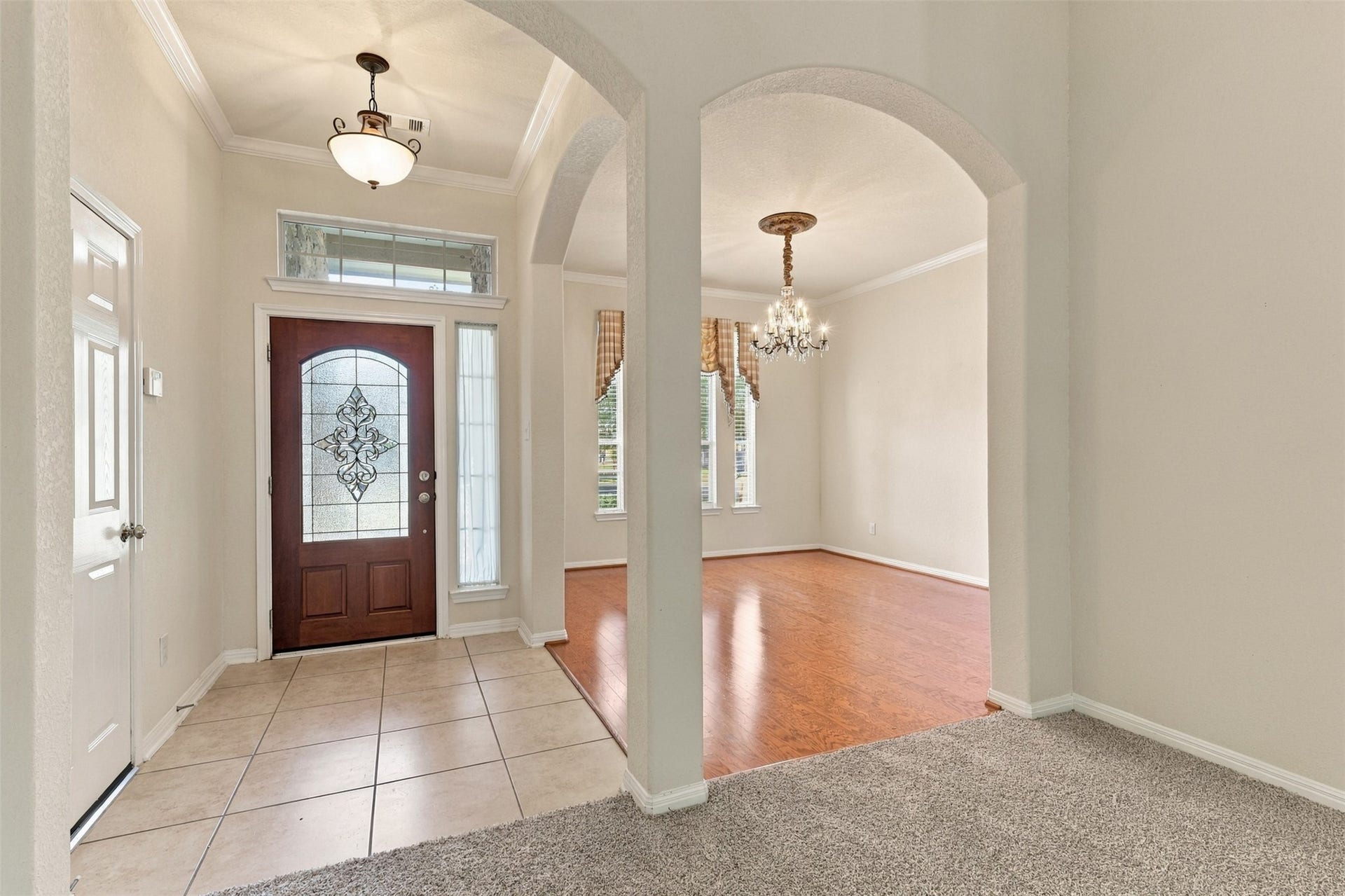 6414 Pinyon Trail Drive, Spring, TX 77389 Elegant entryway with a stunning wooden door featuring decorative glass, leading to a bright dining area with hardwood floors and a classic chandelier.