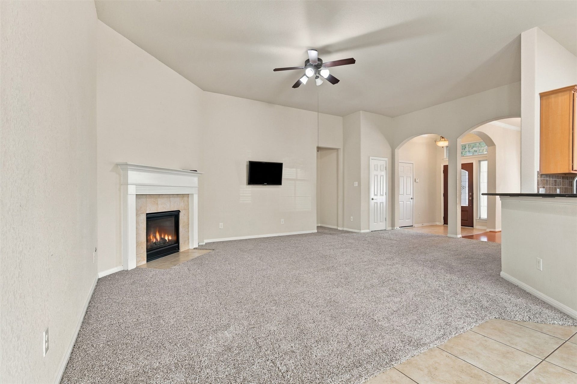 6414 Pinyon Trail Drive, Spring, TX 77389 Another view of the living room featuring a cozy fireplace, plush carpeting, and elegant arched doorways leading to additional living areas.