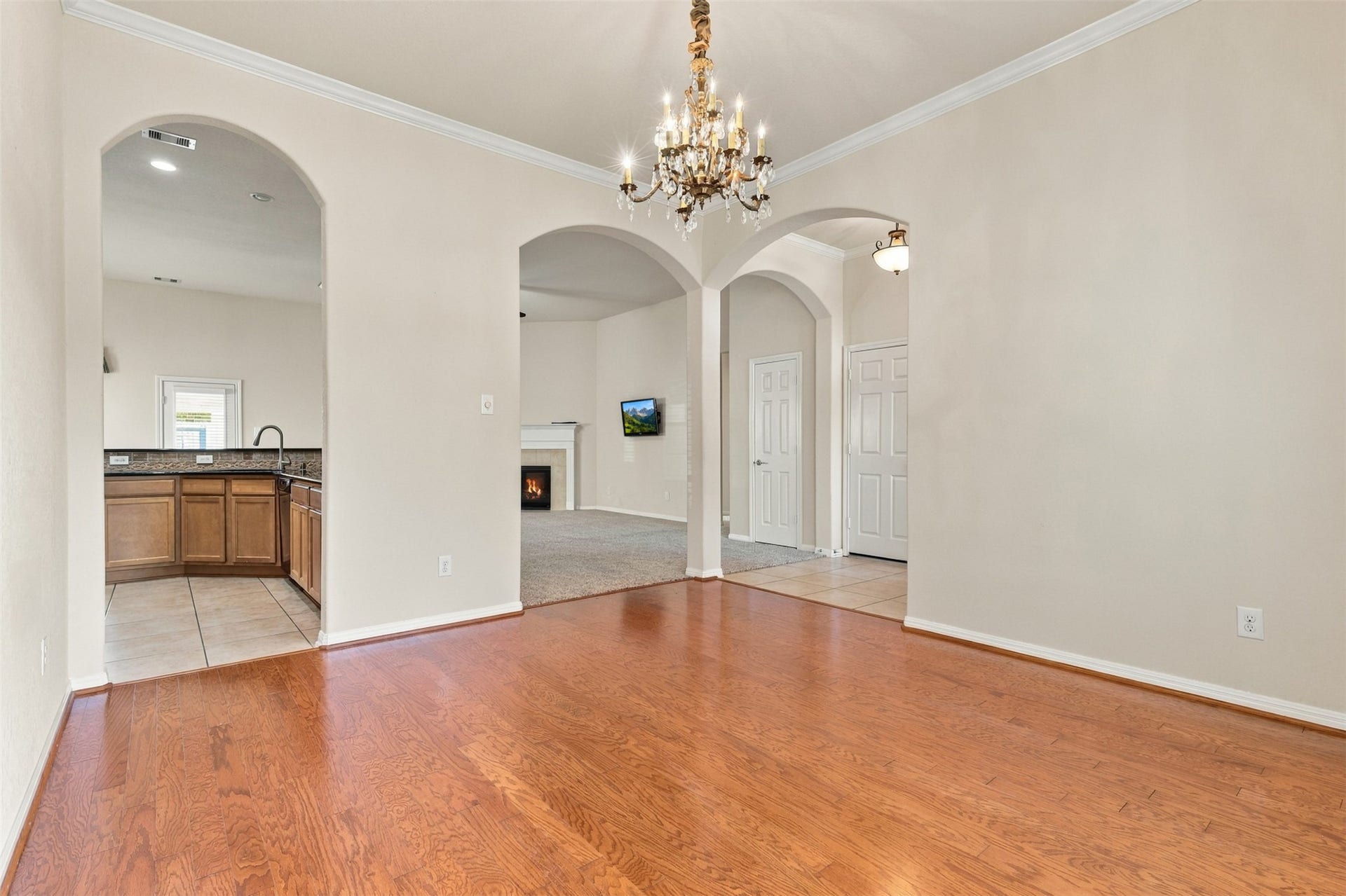 6414 Pinyon Trail Drive, Spring, TX 77389 Another view of the dining rooms with hardwood floors, an ornate chandelier, and arched doorways leading to a cozy kitchen and living area with a fireplace.