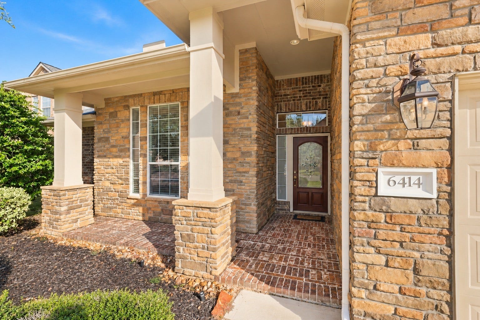 6414 Pinyon Trail Drive, Spring, TX 77389 Stone and brick facade with an inviting covered entryway and elegant glass front door, enhanced by classic lantern-style lighting.