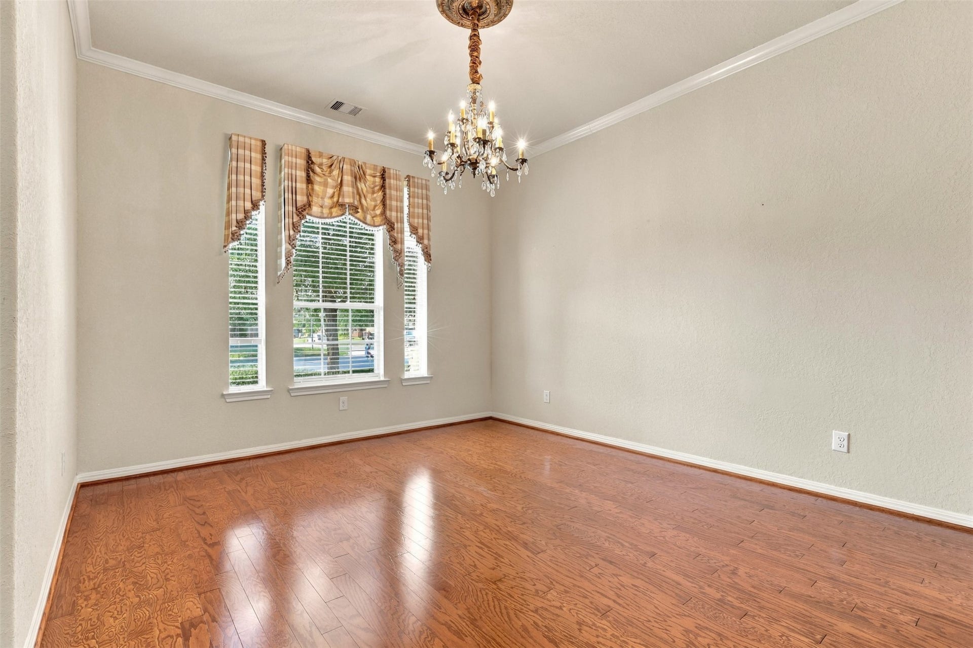 6414 Pinyon Trail Drive, Spring, TX 77389 Elegant dining room featuring rich hardwood floors, a charming chandelier, and large windows with classic drapery, offering ample natural light.