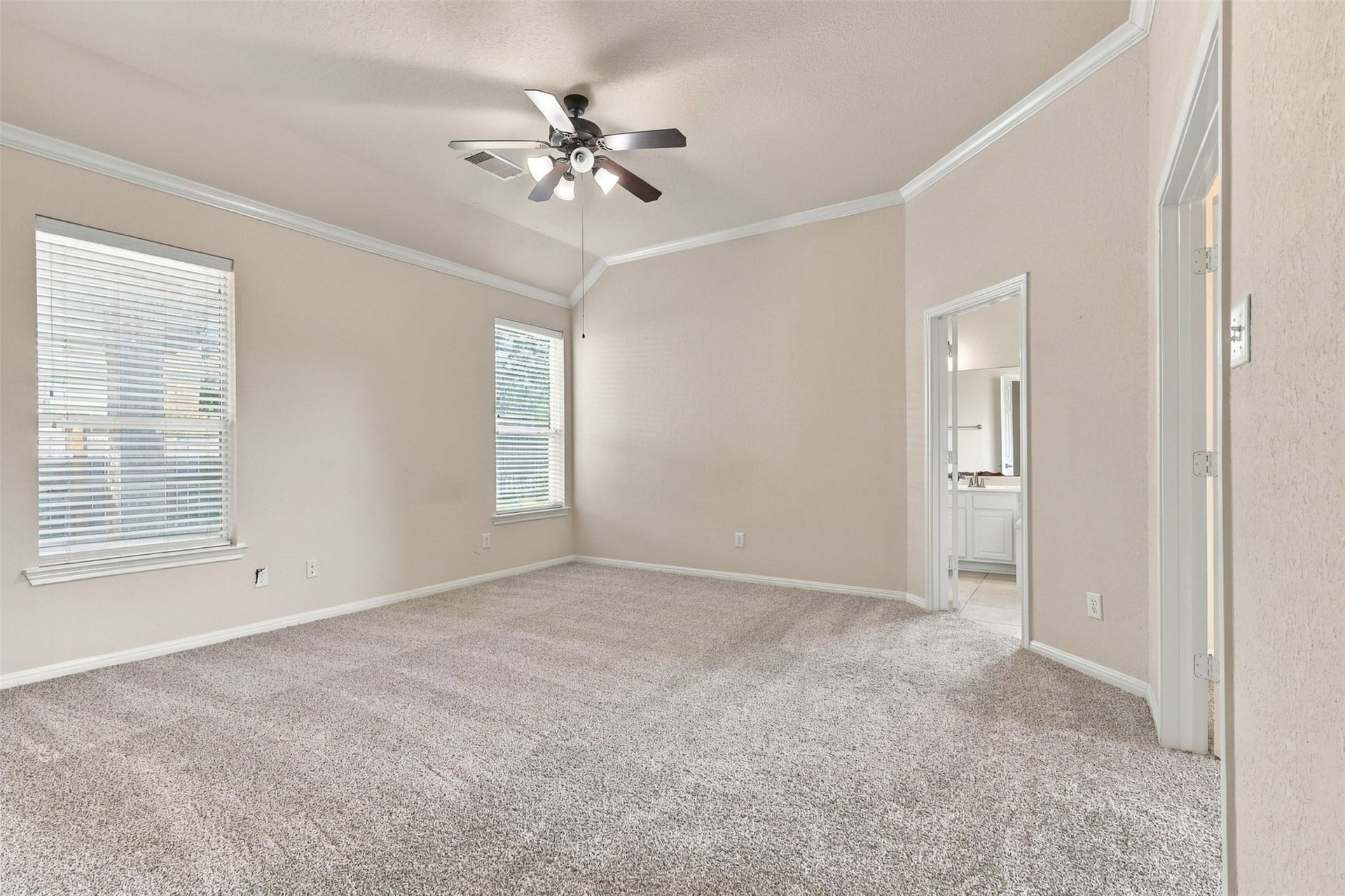 6414 Pinyon Trail Drive, Spring, TX 77389 Spacious primary bedroom with plush carpet, high ceilings, and abundant natural light from large windows, featuring an elegant ceiling fan and direct access to a bright en-suite bathroom.