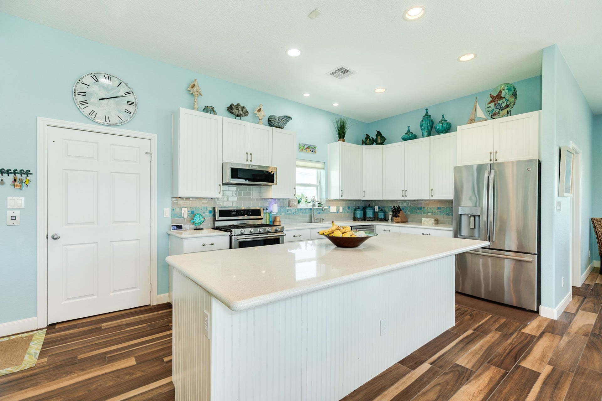 18502 E De Vaca, Galveston, TX 77554 Kitchen view. Flooring throughout the living, dining and kitchen is ceramic plank tile. Kitchen includes a gas range, micro wave, double electric ovens, refrigerator, dishwasher, disposal and an ice machine. The door under the clock is to the elevator.