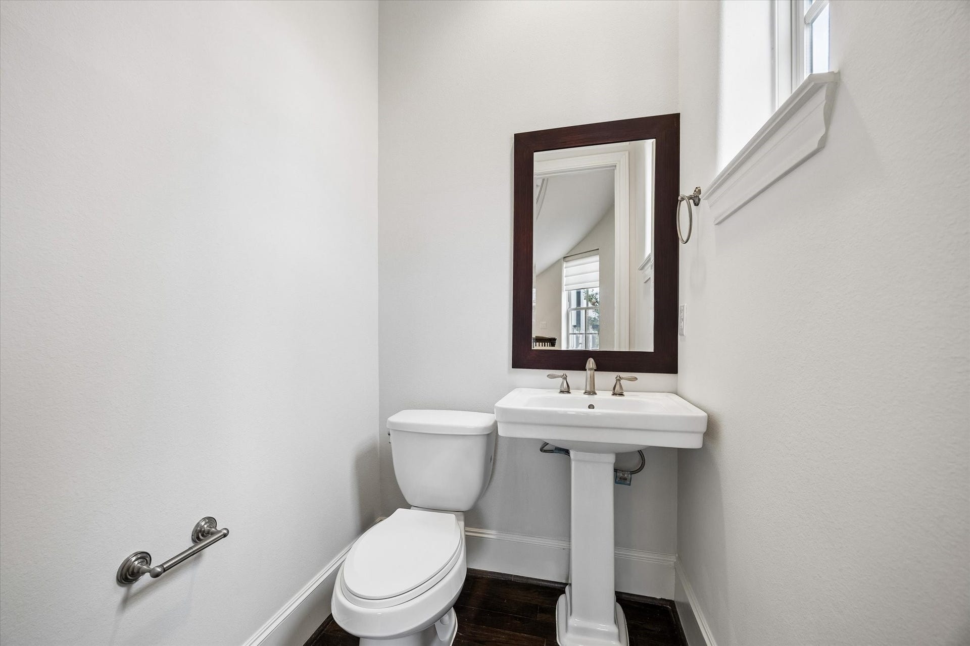 2725 Cohn Garden, Houston, TX 77007 Natural light from a high window brightens the powder bath, finished with a classic pedestal sink, framed mirror, and hardwood flooring.