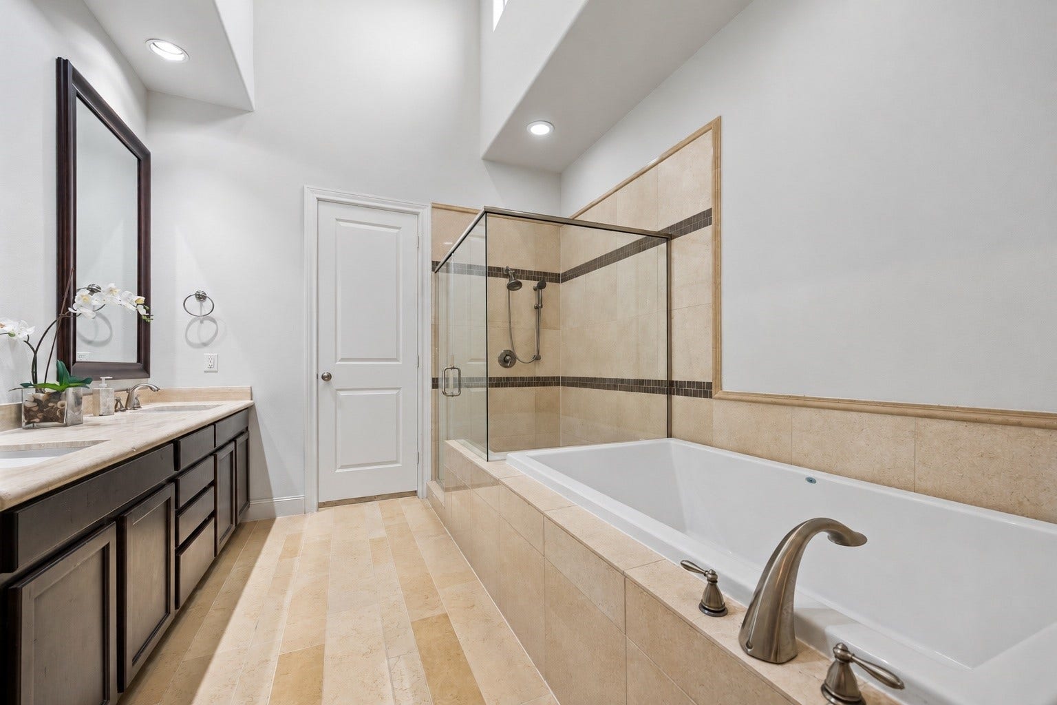2725 Cohn Garden, Houston, TX 77007 A spacious primary bath pairs warm stone tile with dark cabinetry and a dramatic vaulted ceiling. An oversized soaking tub and separate glass enclosed shower create a comfortable retreat, with direct access to one of the two primary closets.