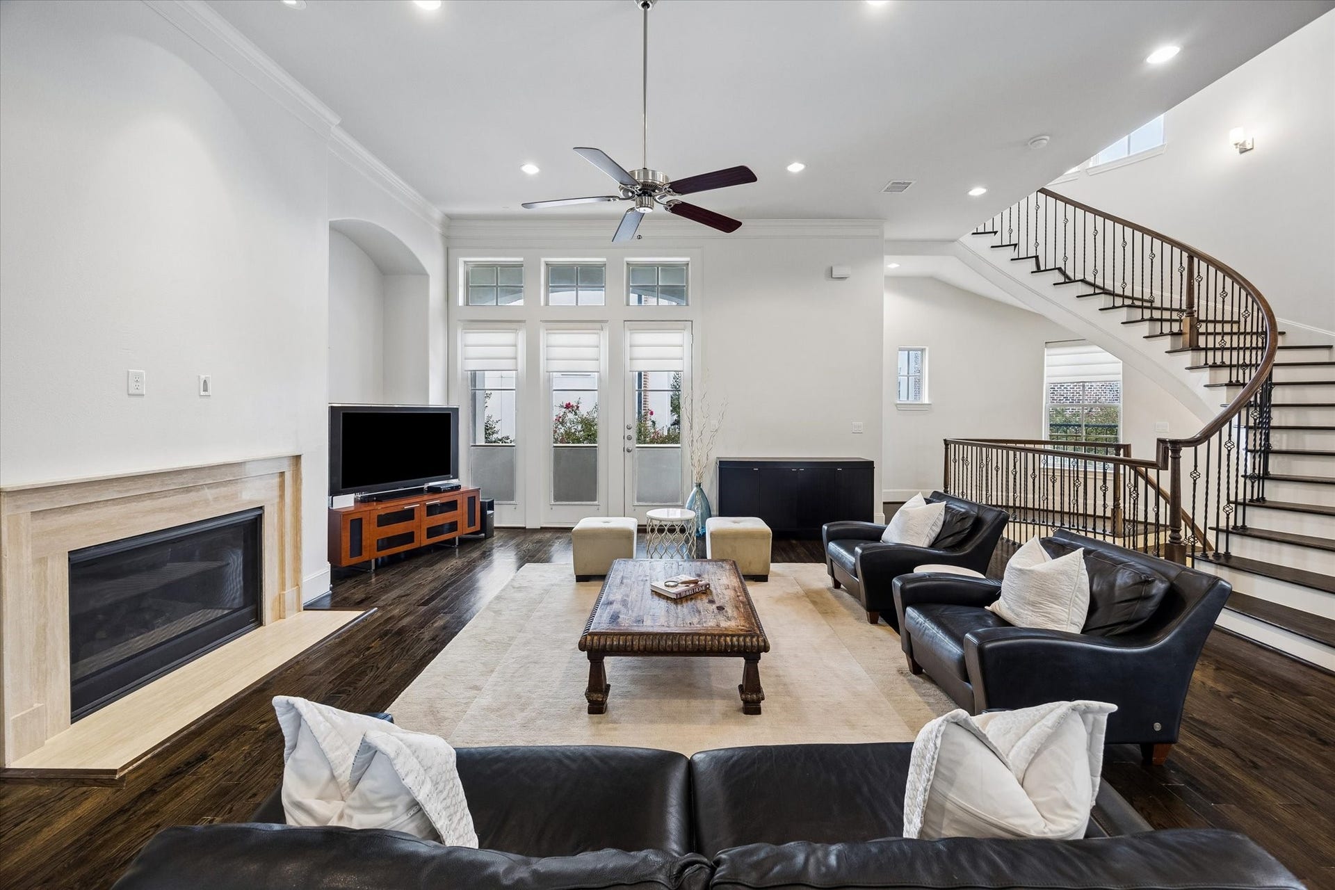 2725 Cohn Garden, Houston, TX 77007 Natural light fills the living room, where rich hardwood floors and a stone fireplace bring warmth to the open layout. French doors and the sweeping staircase add architectural interest while connecting the homes main living spaces.
