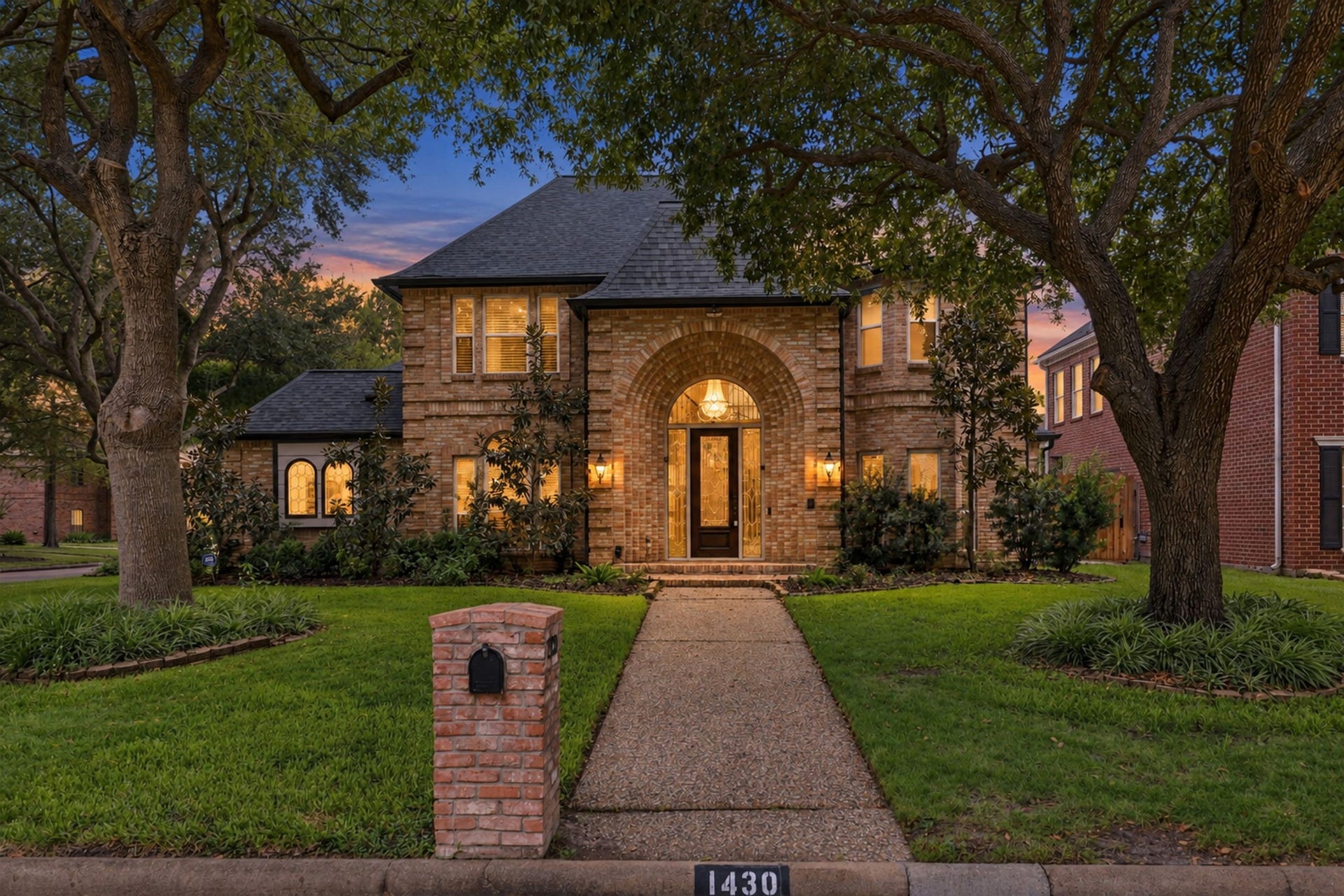 1430 Stependale Drive, Katy, TX 77450 Stunning brick exterior illuminated at dusk, showcasing the elegant arched entryway and mature trees.