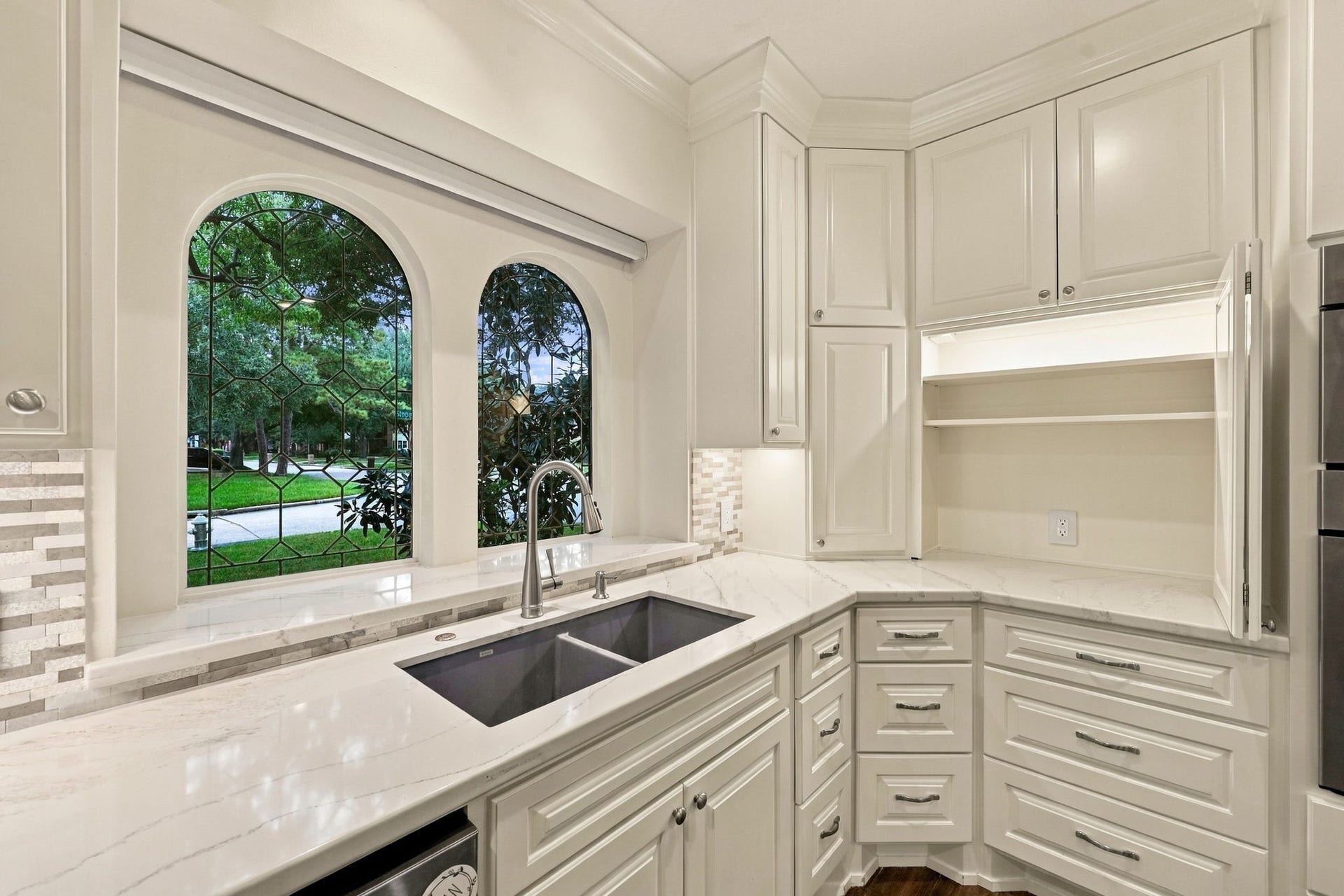1430 Stependale Drive, Katy, TX 77450 Kitchen sink positioned beneath elegant arched windows, complemented by white cabinetry and stone countertops.
