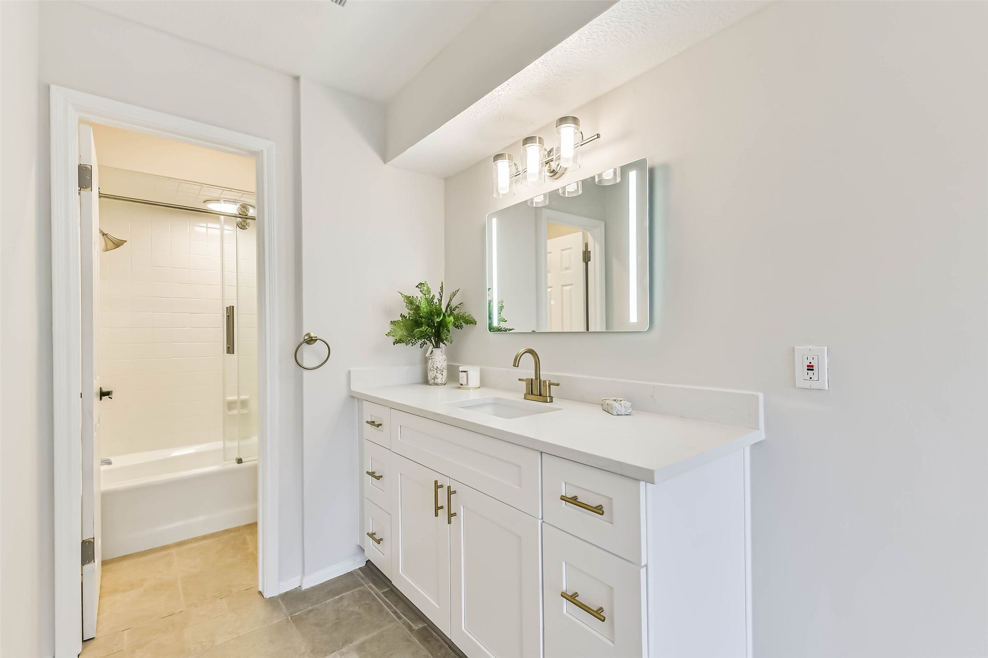The second full bathroom showcases quartz counters. shaker style cabinetry with gold fixtures, updated light fixture and a tub+shower duo.