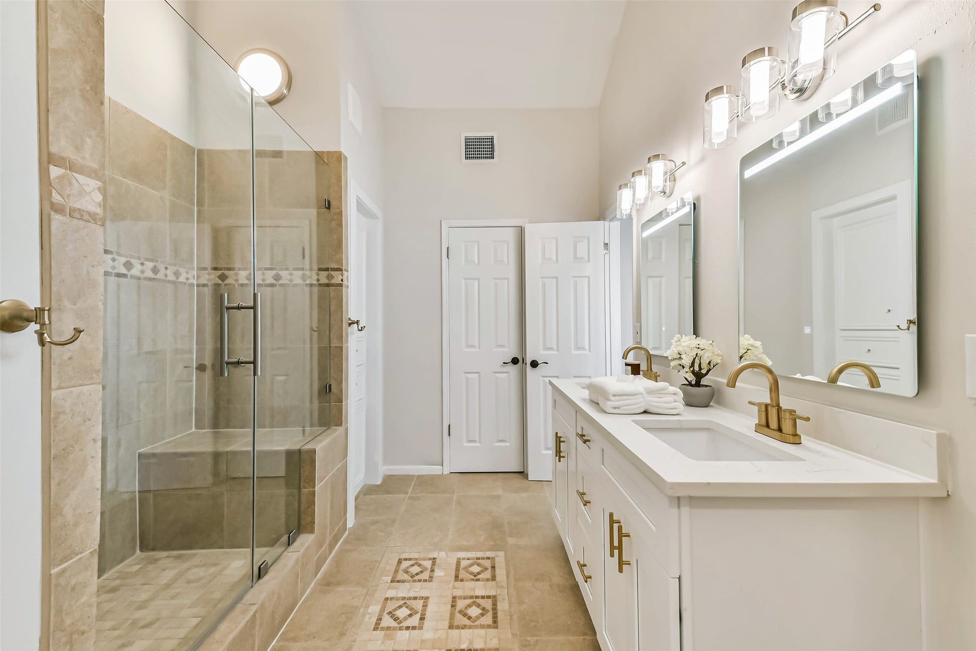 The primary bathroom has been updated with shaker style cabinetry, gold fixtures, quartz counters and LED mirrors.