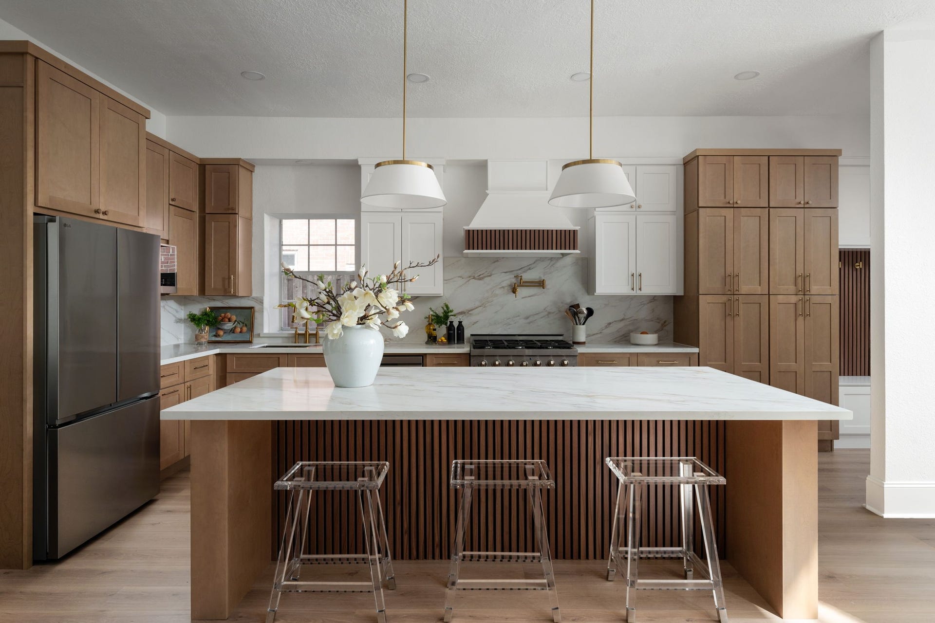 The oversized island creates a central gathering space within the kitchen, offering additional seating, prep space, and everyday functionality. Warm wood cabinetry and clean-lined finishes balance the homes classic architecture with modern design. The layout opens directly into the surrounding living areas for easy entertaining.