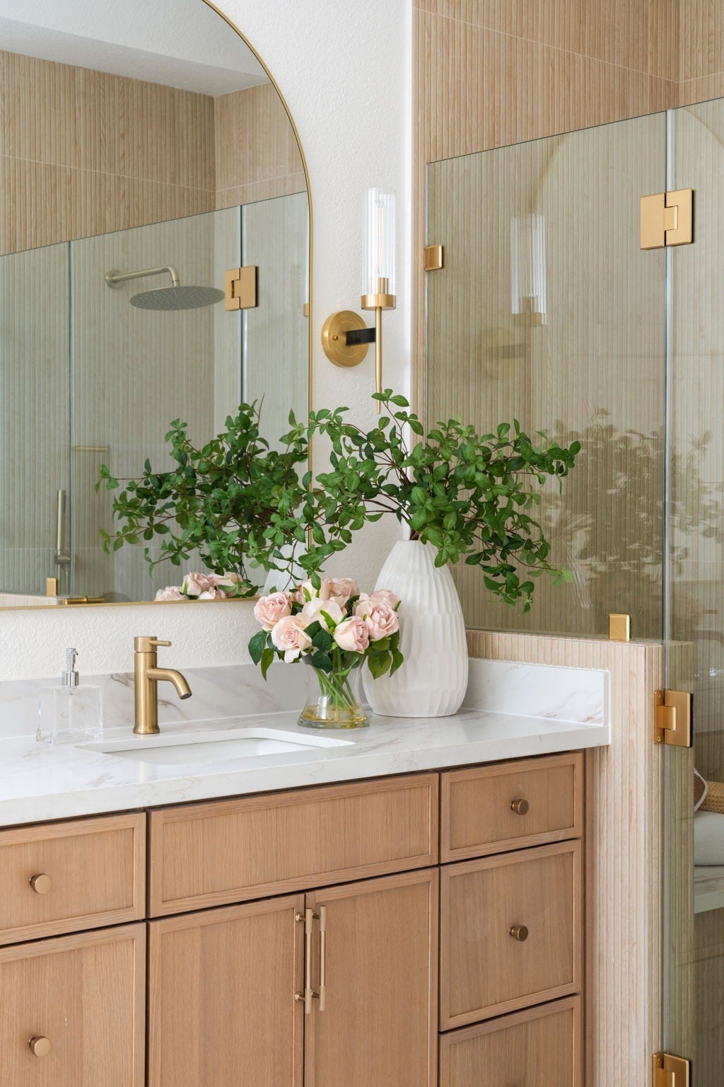 Warm wood cabinetry, quartz surfaces, and arched mirrors create a refined vanity space within the primary bath. Designer lighting and brass fixtures continue throughout the rooms updated finishes. Large windows bring additional natural light into the bath area.