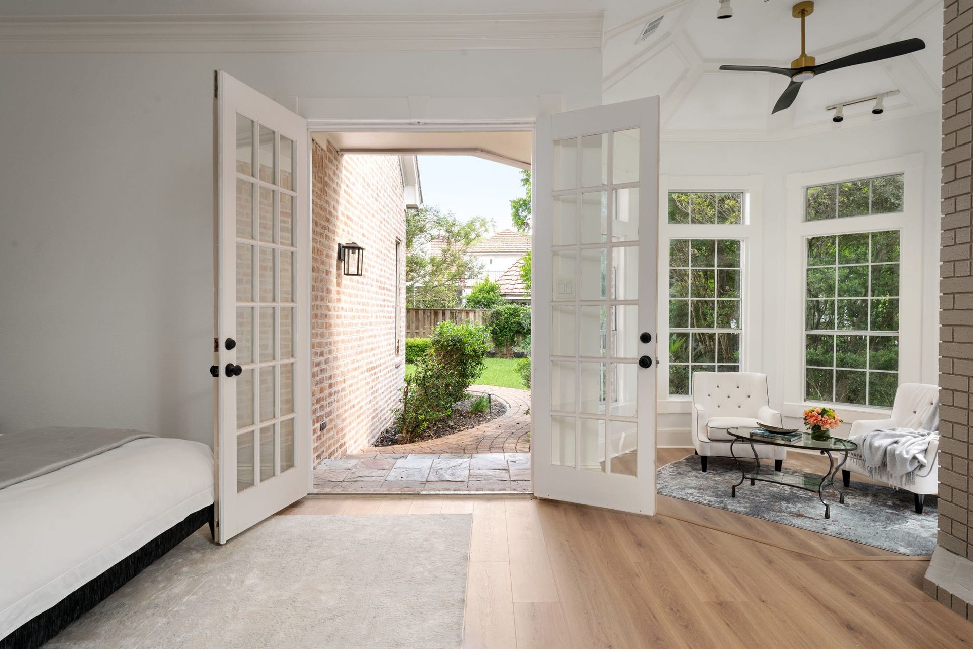 Positioned within its own private wing, the primary suite offers strong indoor-outdoor connection through expansive windows and direct patio access. The layout includes additional space for seating or lounge areas near the decorative fireplace feature. Contemporary finishes and updated flooring continue throughout the room.