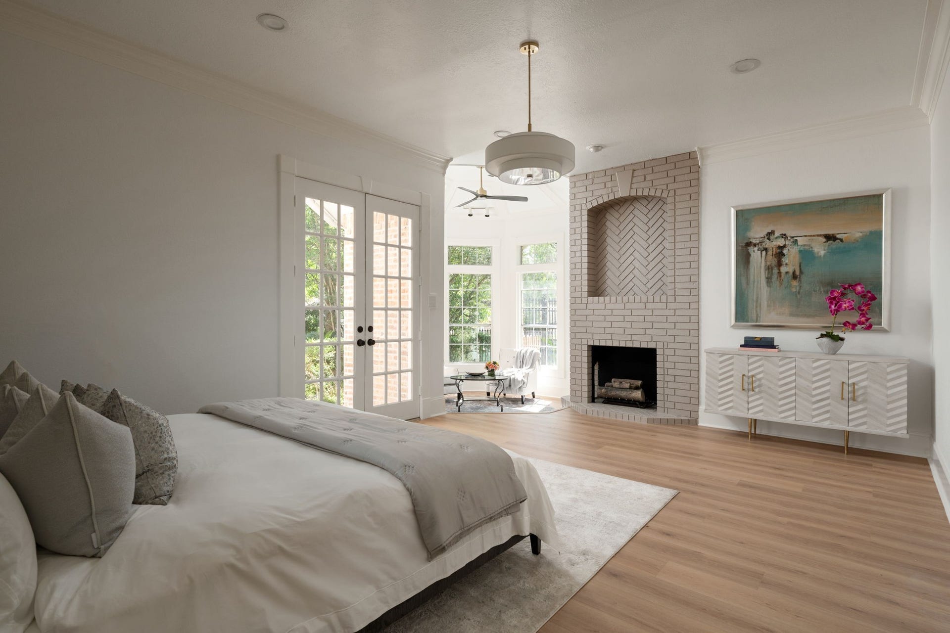 The first-floor primary suite offers a spacious layout with updated flooring, elevated ceilings, and natural light throughout the room. A decorative fireplace feature anchors the sitting area while maintaining connection to the outdoor spaces, while a nearby utility room adds everyday convenience to the primary wing. Large windows and updated finishes create a bright and private retreat.