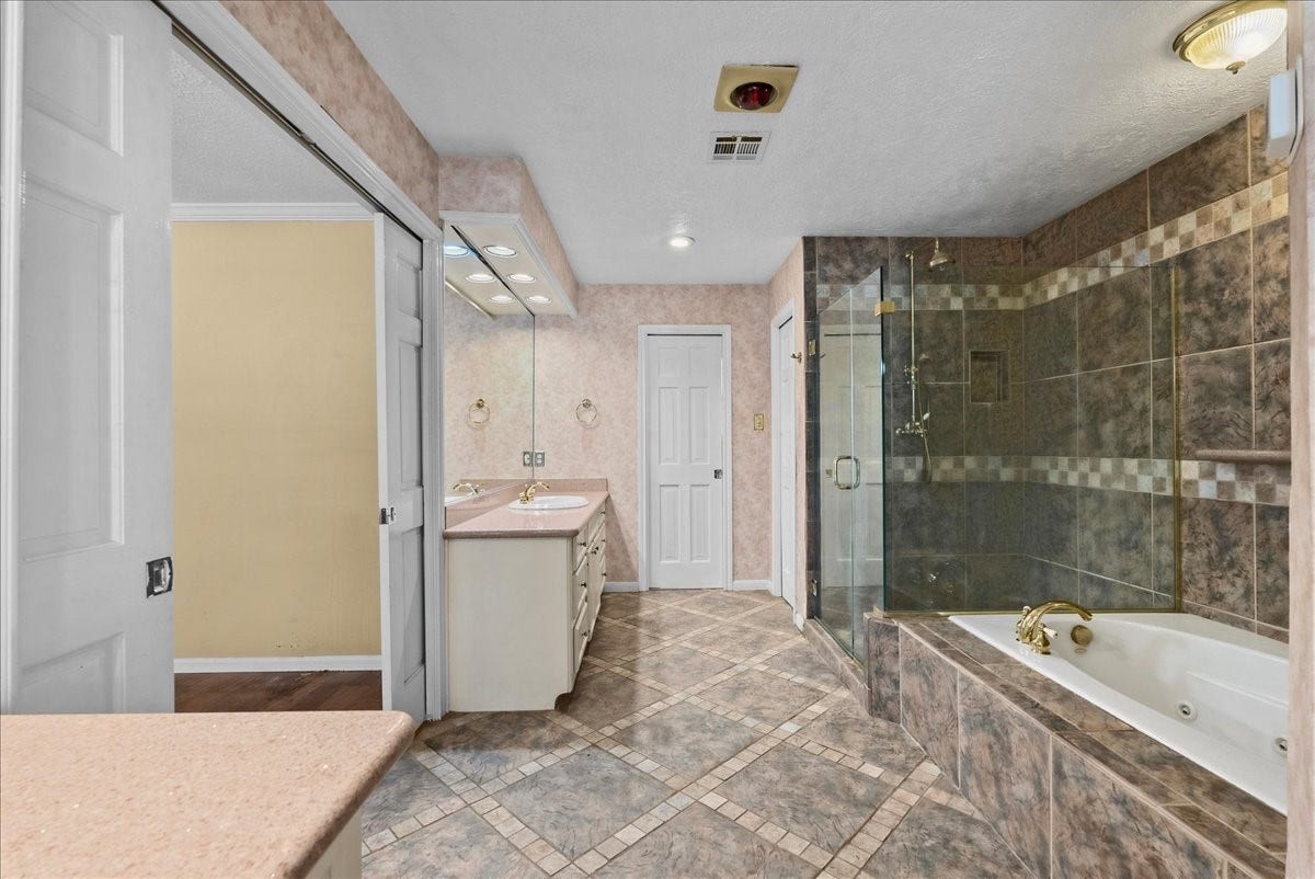 Indulge in luxury with a spacious primary bathroom featuring elegant tile work, a glass-enclosed shower, and a relaxing jetted tub for ultimate comfort.
