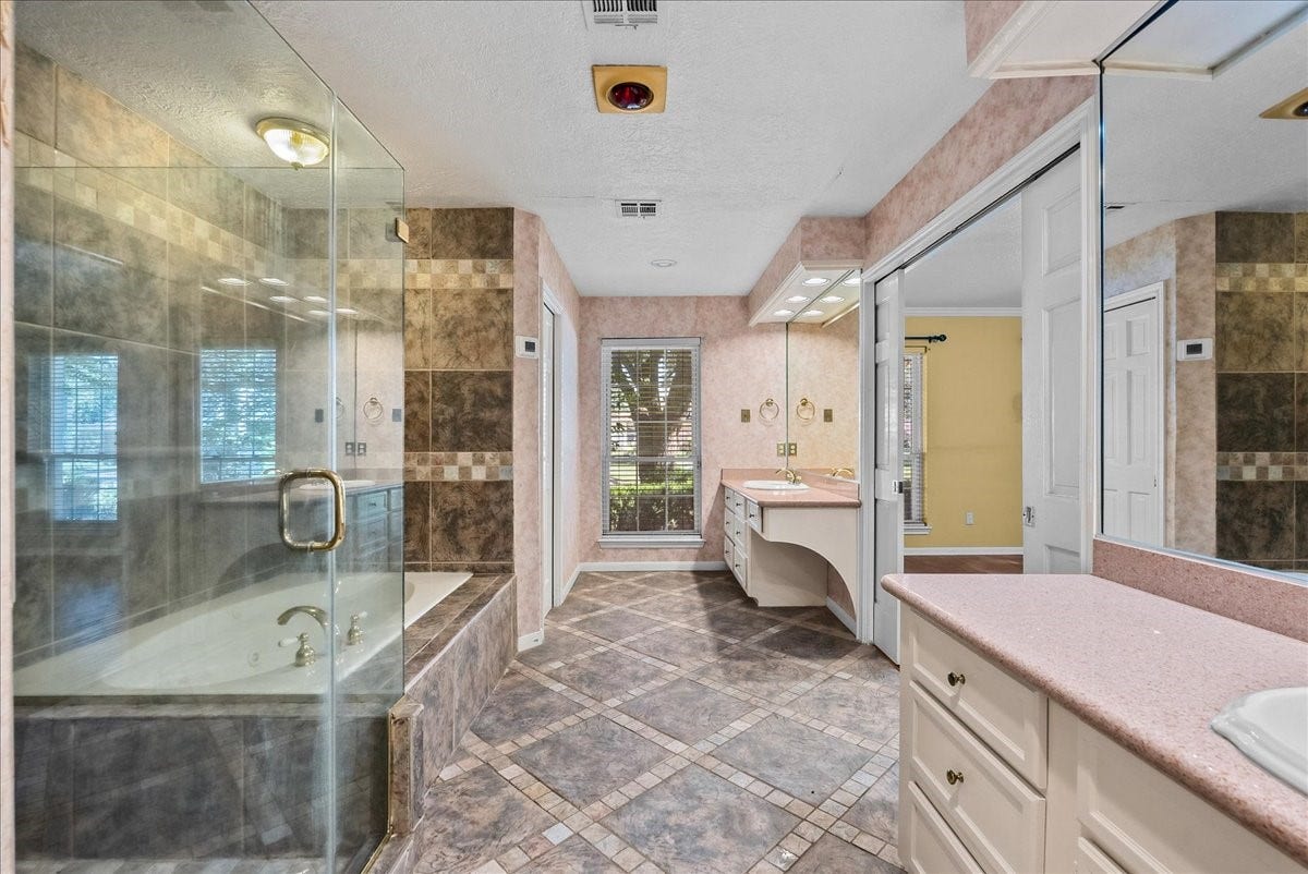 Luxuriate in this elegant primary bathroom featuring a spacious glass-enclosed shower, inviting soaking tub, and dual vanities, all set against stylish tilework and abundant natural light.