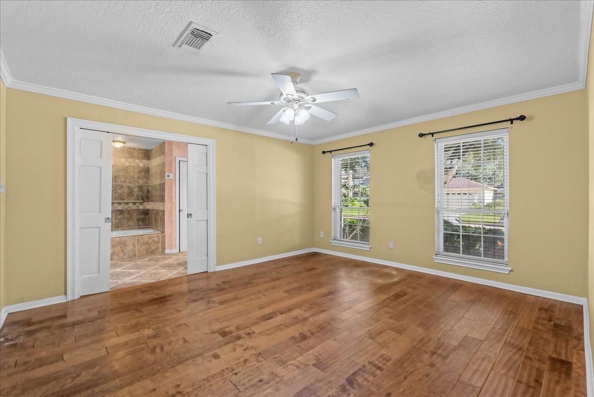 Spacious and inviting, the primary bedroom features warm hardwood floors, abundant natural light from large windows, and direct access to a luxurious en-suite bathroom.