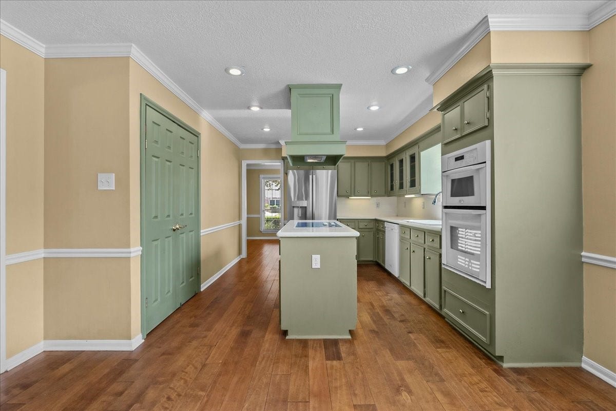 Charming kitchen with sage green cabinets, sleek stainless steel appliances, and warm hardwood floors, offering a perfect blend of style and functionality.