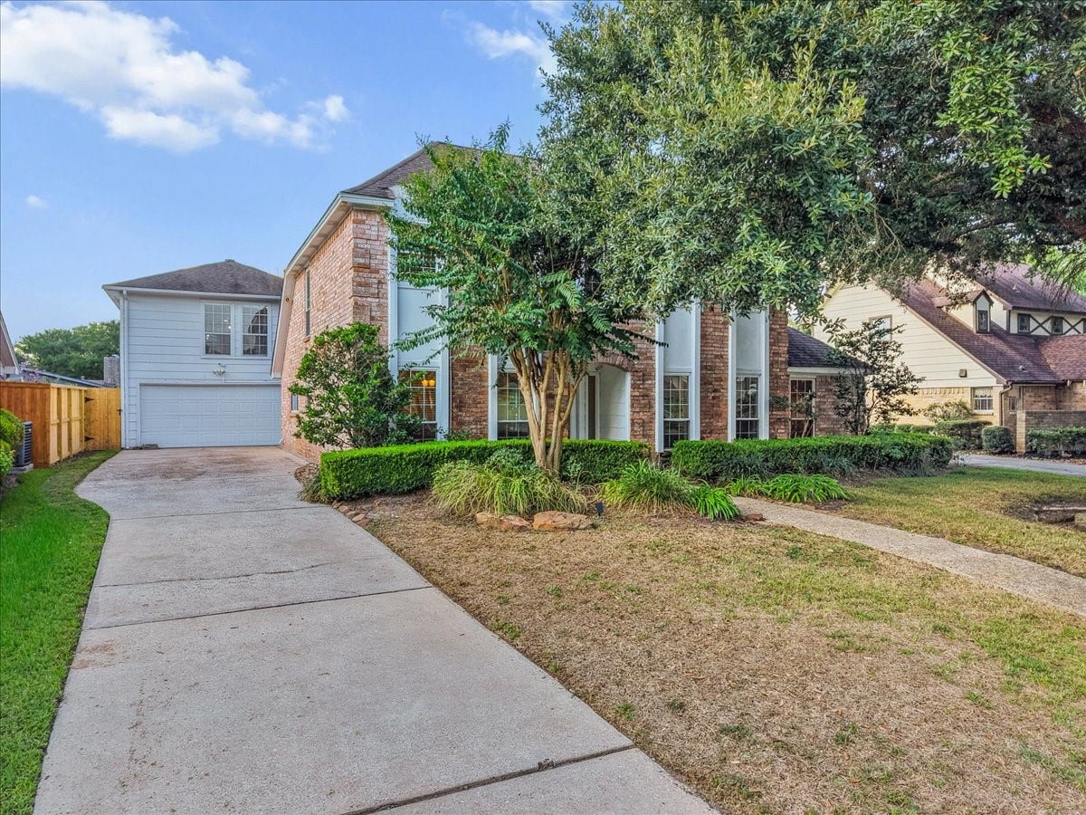 Charming two-story brick home with expansive windows, a well-maintained front yard, and a spacious driveway leading to a two-car garage.