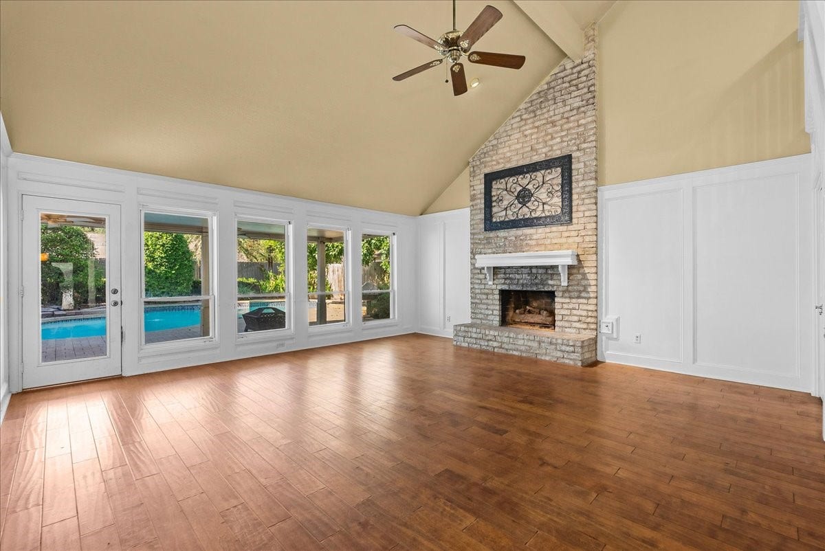 A spacious and inviting living room featuring a charming brick fireplace and abundant natural light from expansive windows overlooking the pool area.