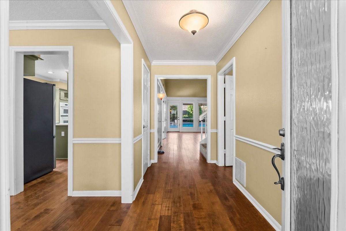 Step into this inviting entryway, where warm wood floors and elegant crown molding set the stage for a welcoming atmosphere, seamlessly leading you toward the heart of the home.